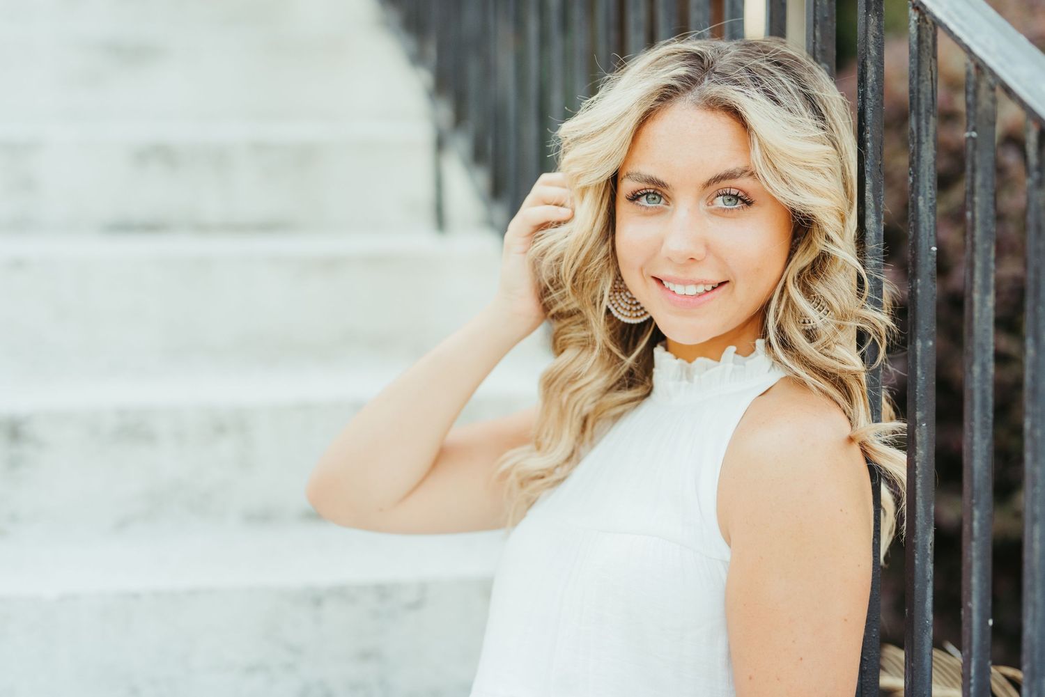 A graduate in a white halter top poses against a staircase railing.