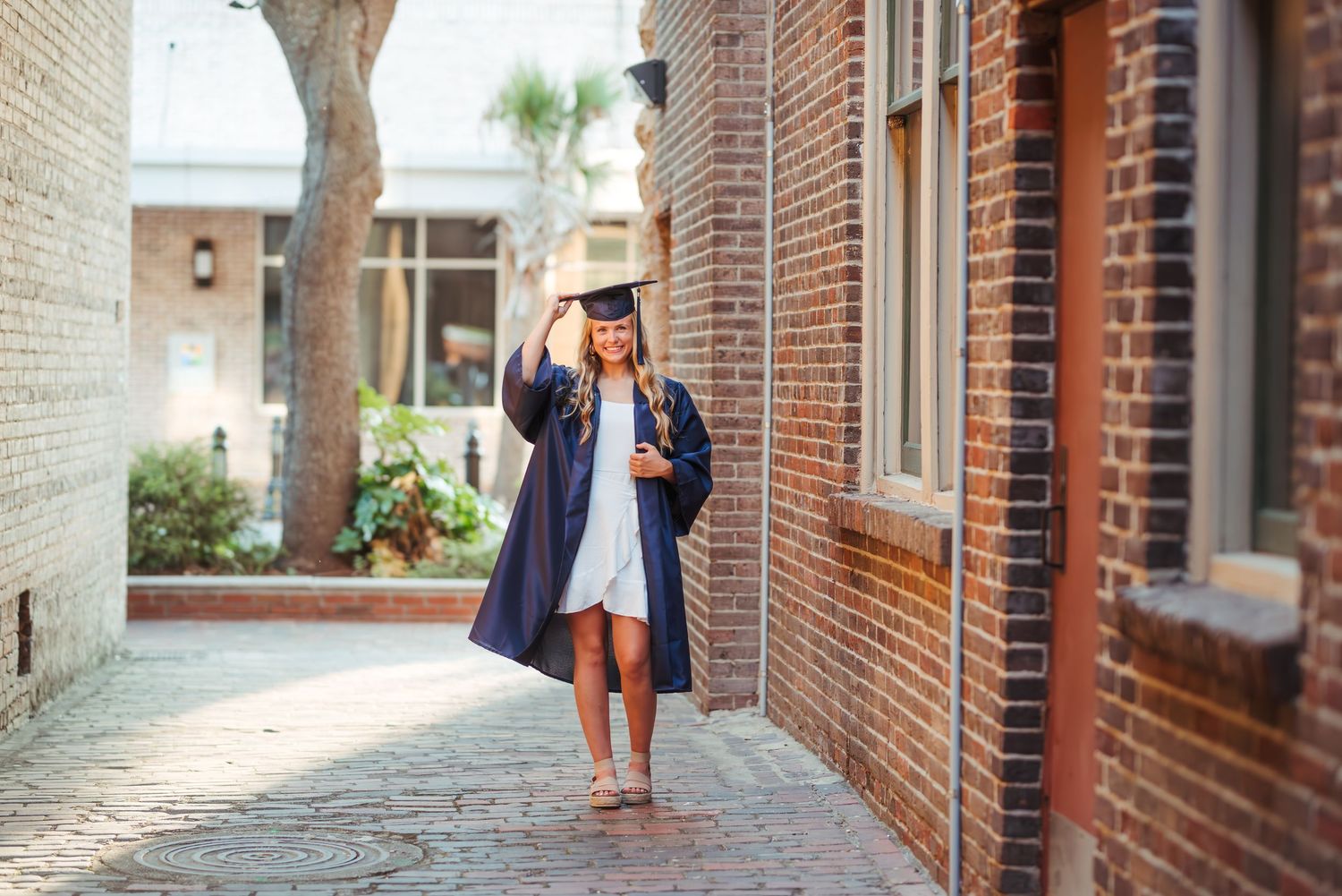 A graduate in academic regalia walks along a brick pathway.