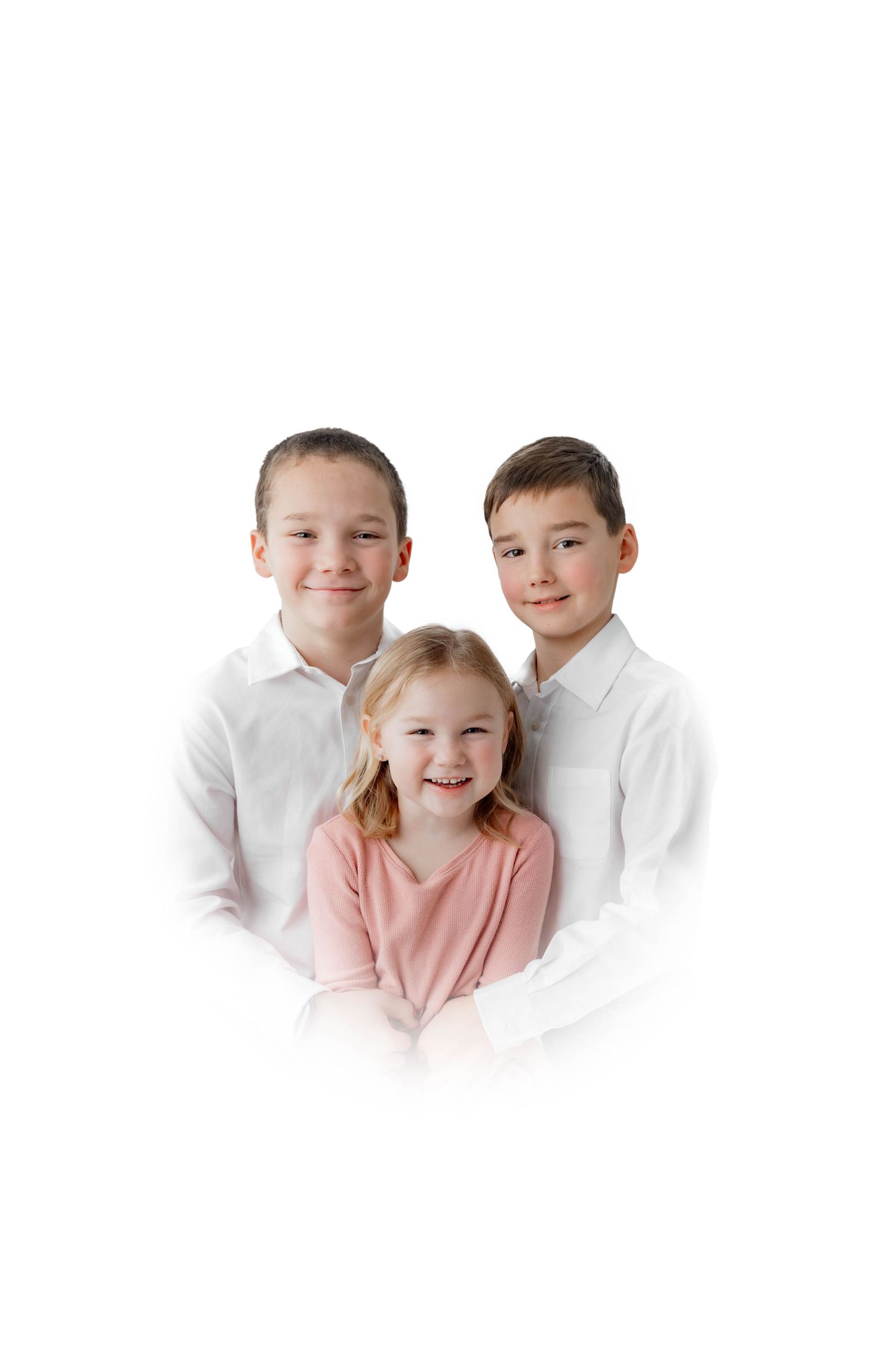 Three smiling children pose together, two boys in white shirts flanking a young girl in pink, against a white background.