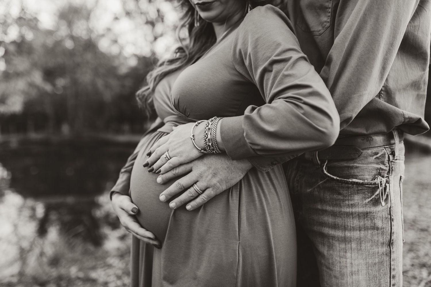 Black and white photo of a couple sharing an intimate maternity moment outdoors.