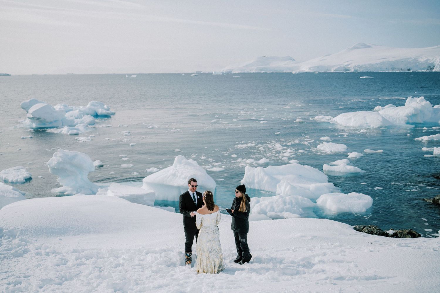 Small ceremony gathering on an ice formation with floating icebergs in the background.