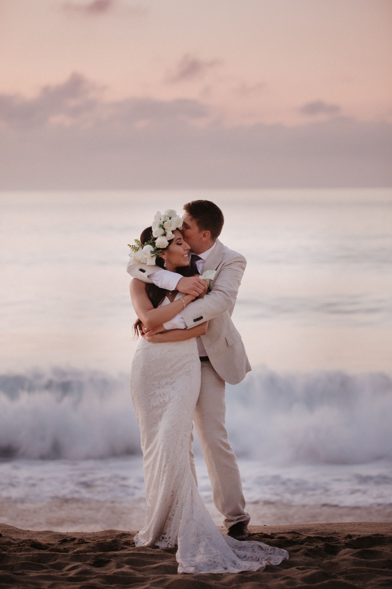 A romantic beach wedding scene at sunset with waves crashing behind the couple.