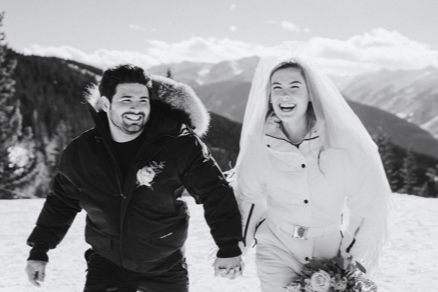 A joyful winter engagement photo with snow-capped mountains in the background.