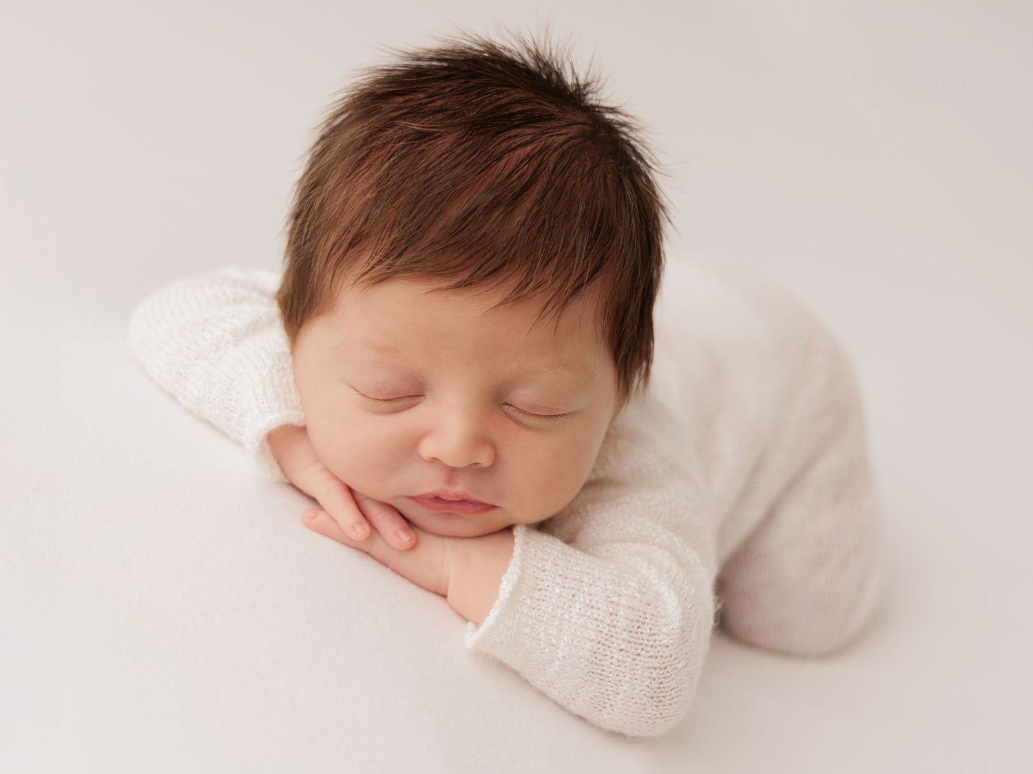 Sleeping newborn baby in soft white knit blanket lies peacefully on light backdrop in composite portrait.