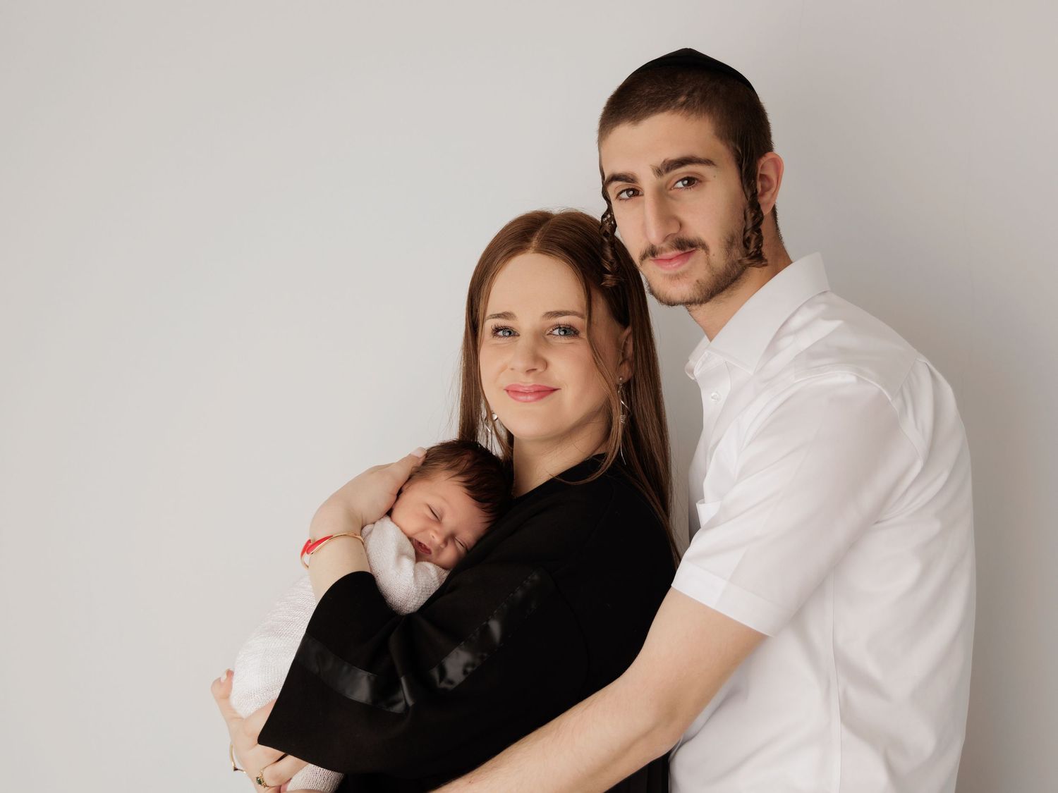 Family with newborn baby pose together against white background in casual black and white outfits for portrait.