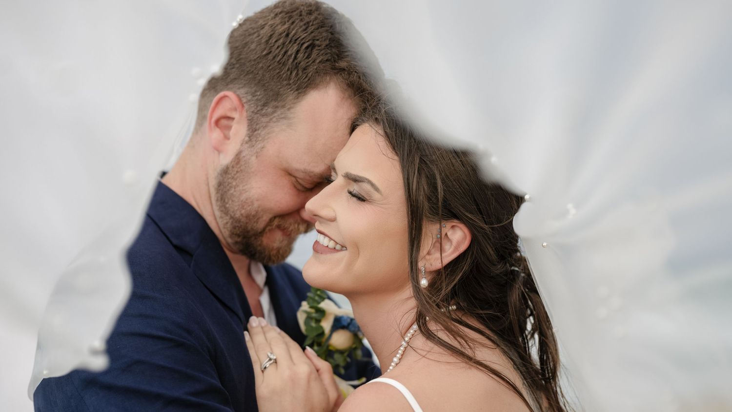 A bride and groom share a romantic moment under a flowing white veil on their wedding day.