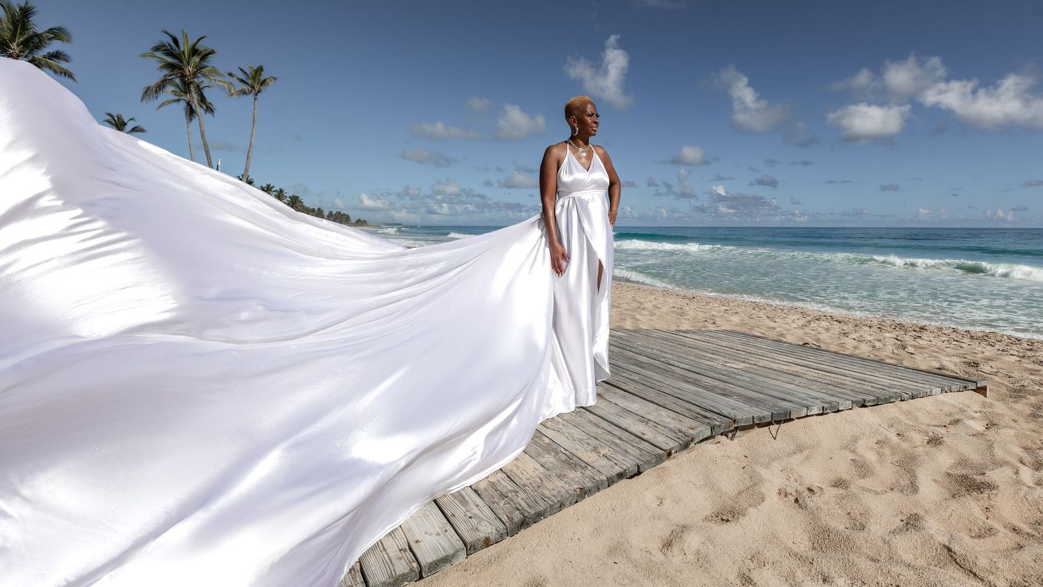 A beautiful beach wedding ceremony setup with white chairs and palm trees along a tropical shoreline at sunset.