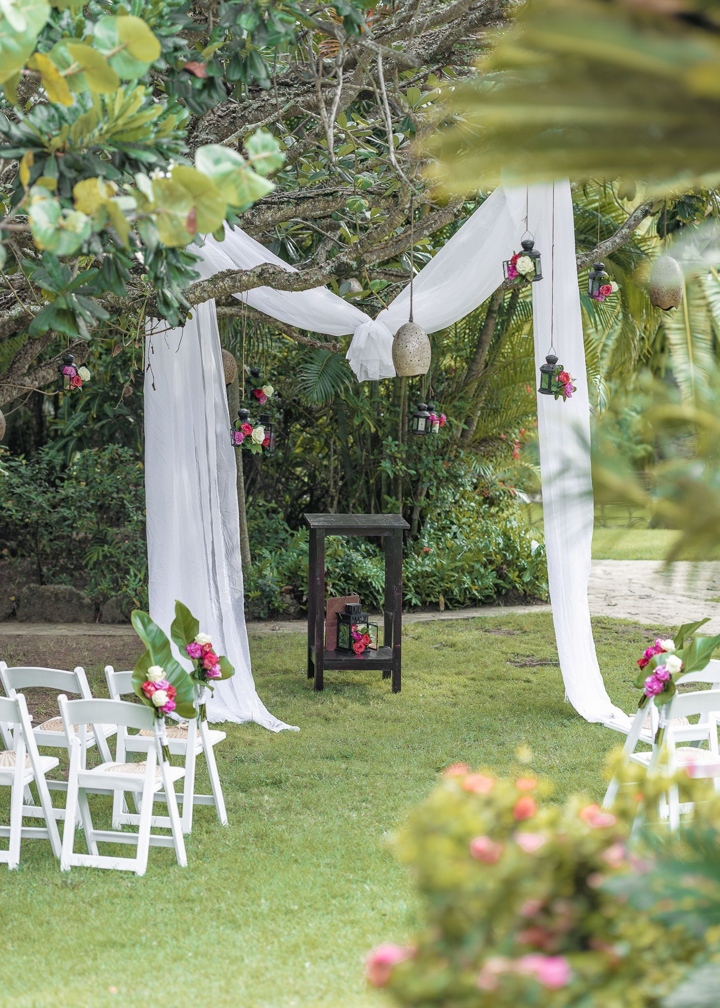 White fabric drapes and folding chairs create an elegant outdoor wedding ceremony setup in a garden setting.