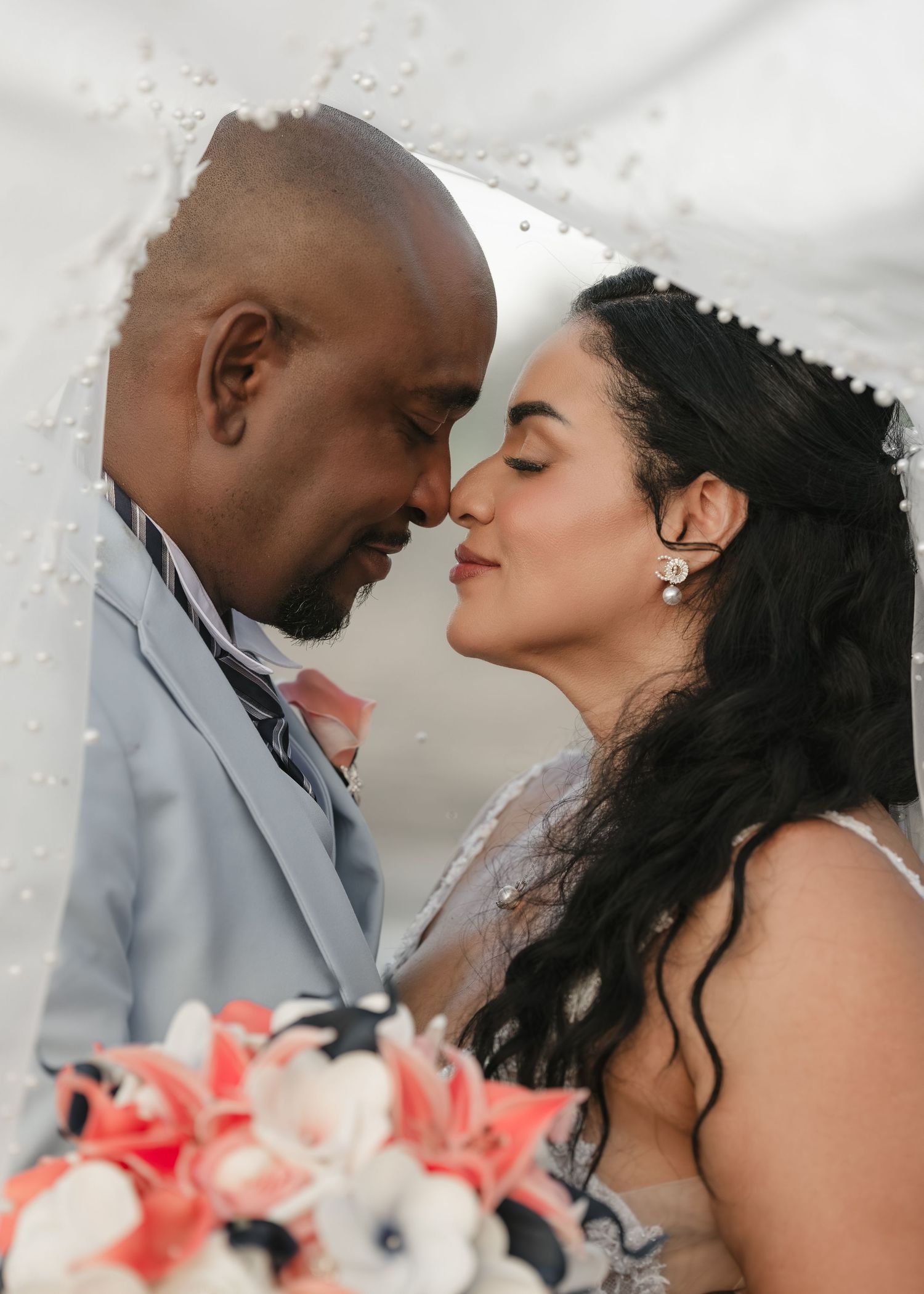 A romantic couple shares intimate moments in a wedding photoshoot sequence with coral-colored flowers in the foreground.