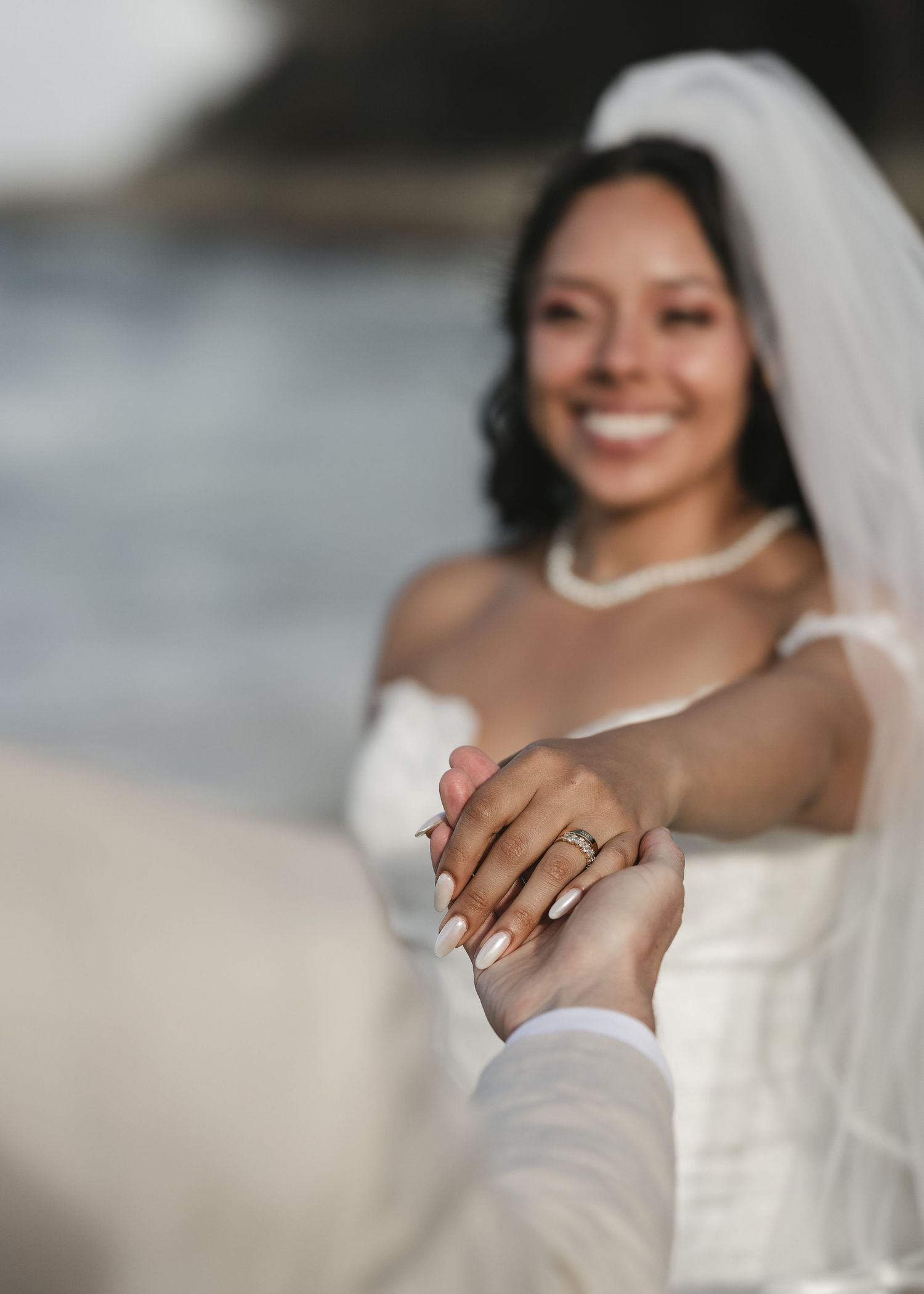 A bride wearing a white wedding dress shows off her engagement ring and wedding band in a close-up shot.