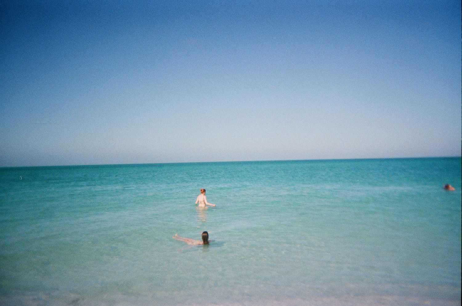 Two swimmers enjoy the calm turquoise waters of a sunny beach on a clear day.