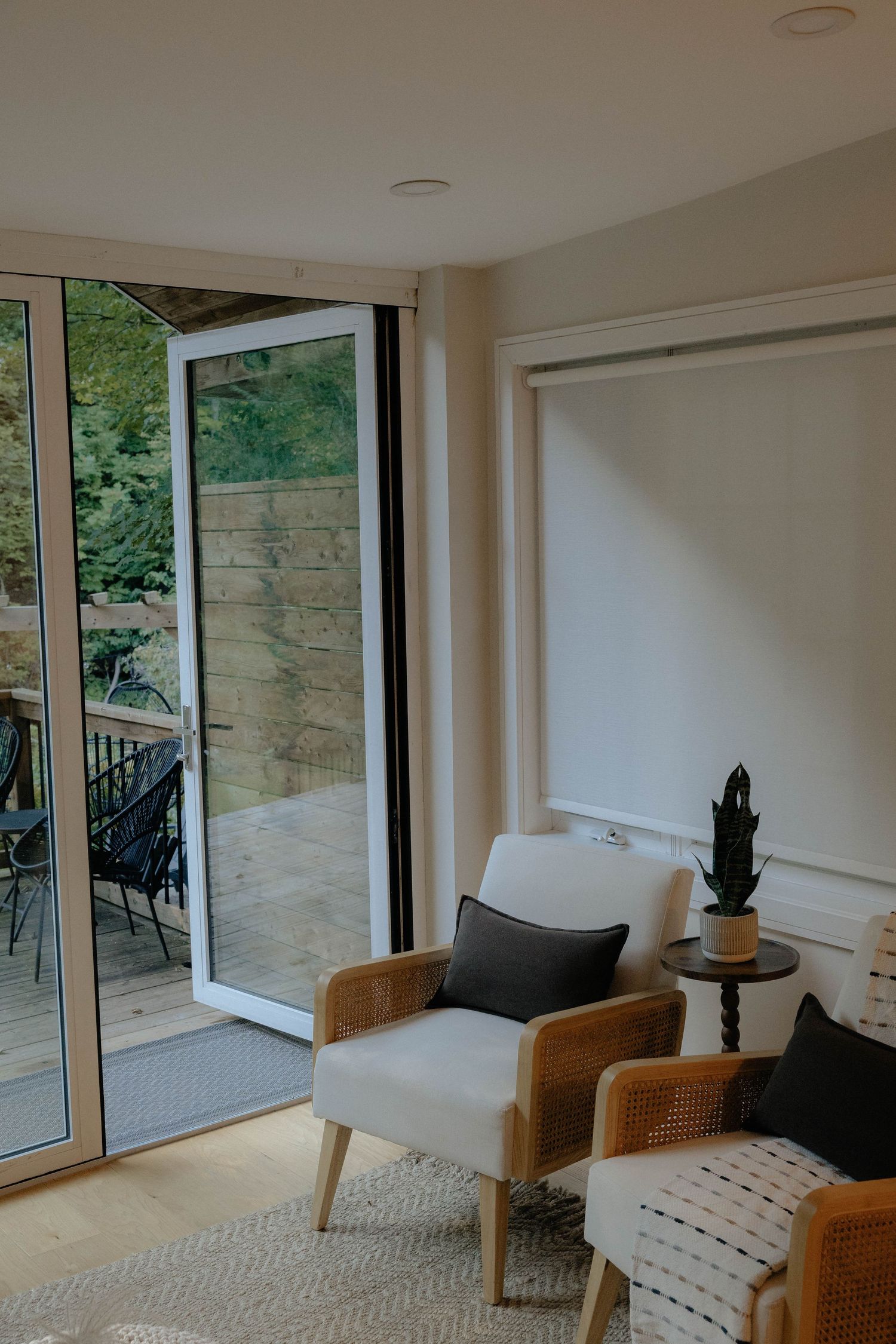 Modern living room with white armchair, rattan furniture, and open glass doors leading to a garden patio.