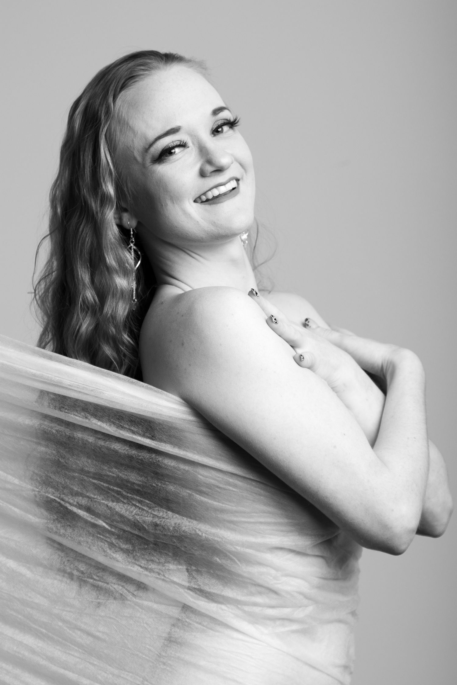Black and white portrait of a smiling woman wrapped in transparent plastic wrap wearing a necklace. Boudoir photography Christchurch