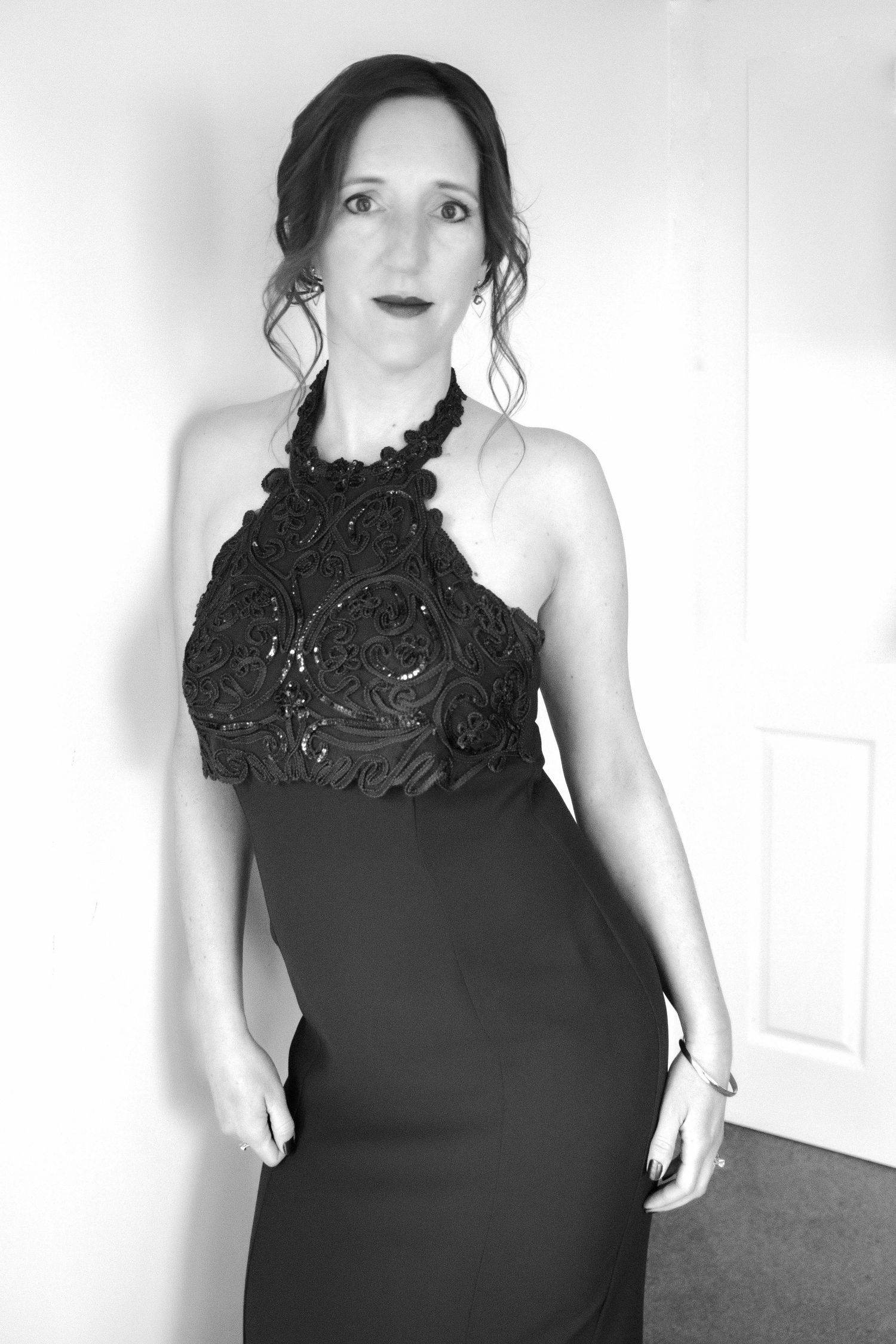 Black and white photo of a woman in an elegant halter neck gown with floral embroidery, posing indoors. Portrait photography Christchurch