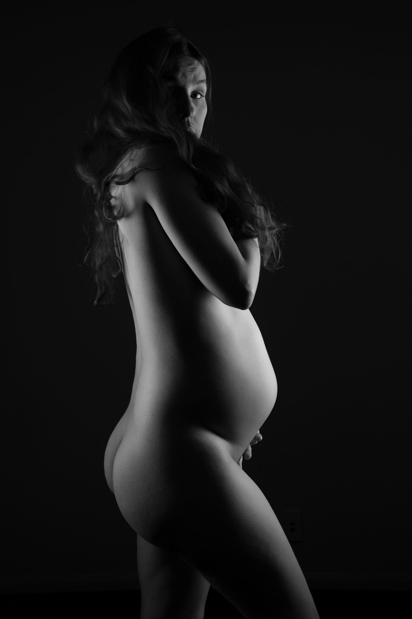 Black and white artistic nude silhouette of pregnant woman posing gracefully against dark background. Boudoir photography Christchurch