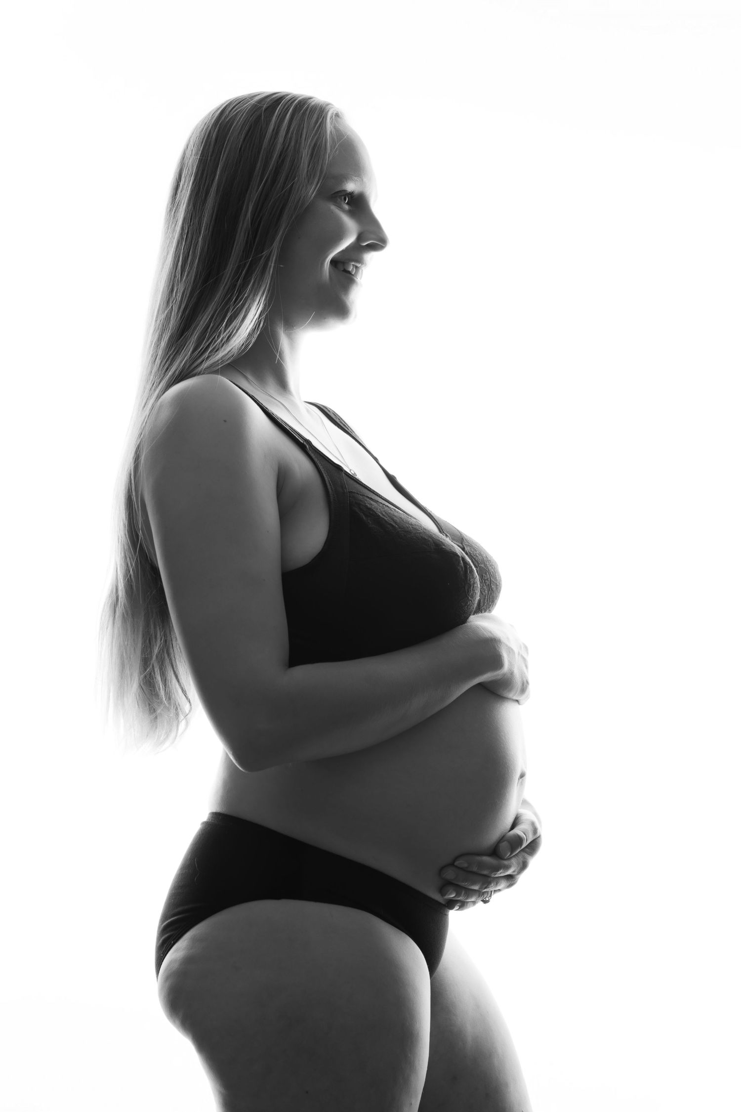 Black and white side profile of smiling pregnant blonde woman in black bikini cradling baby bump. Boudoir photography Christchurch maternity