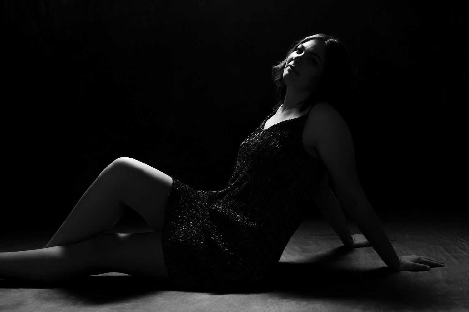 Artistic black and white silhouette of a woman in a lace dress posing dramatically on a dark studio floor. portrait photography Christchurch