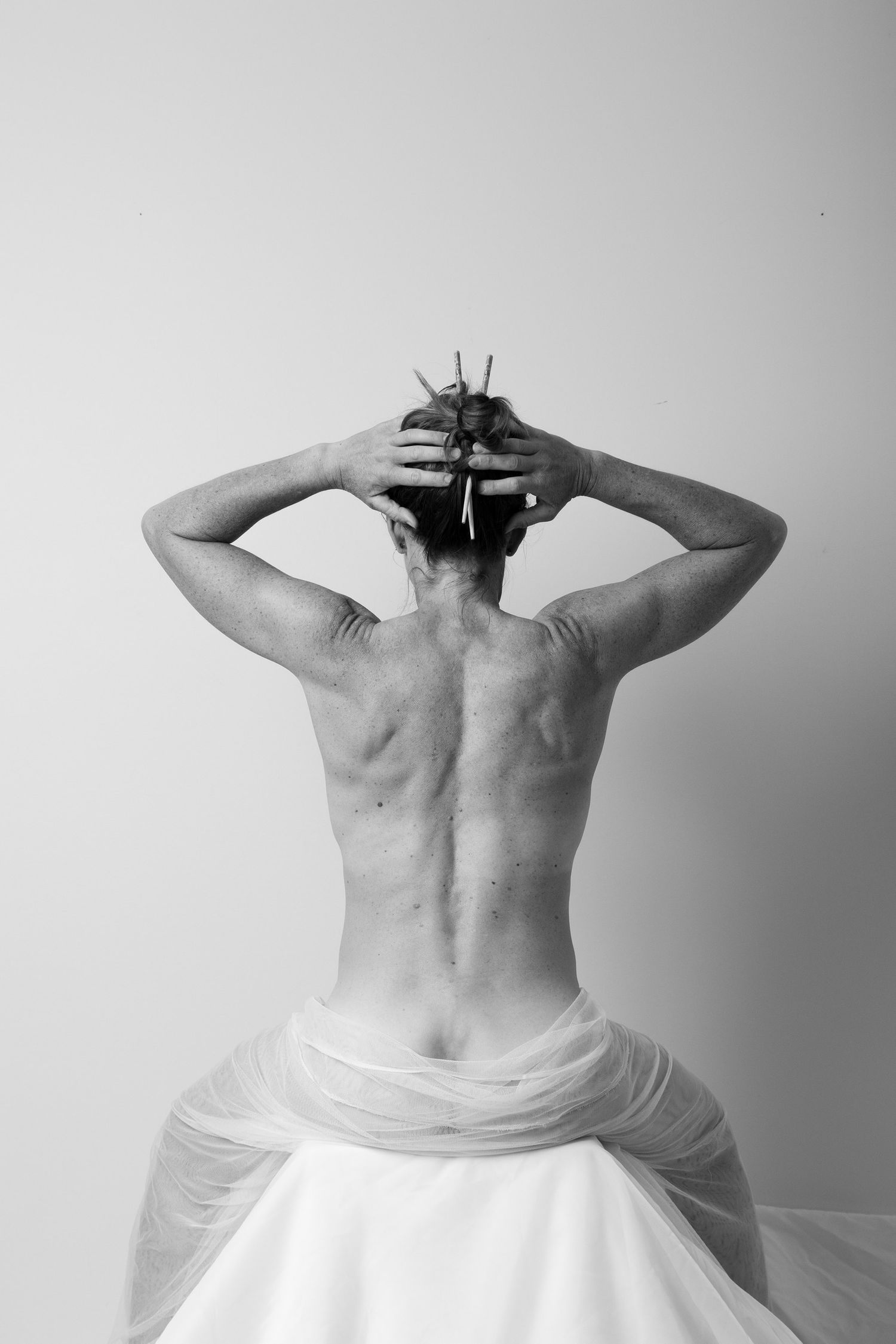 Black and white artistic rear view of person with hands on head draped in white fabric. Boudoir photography Christchurch