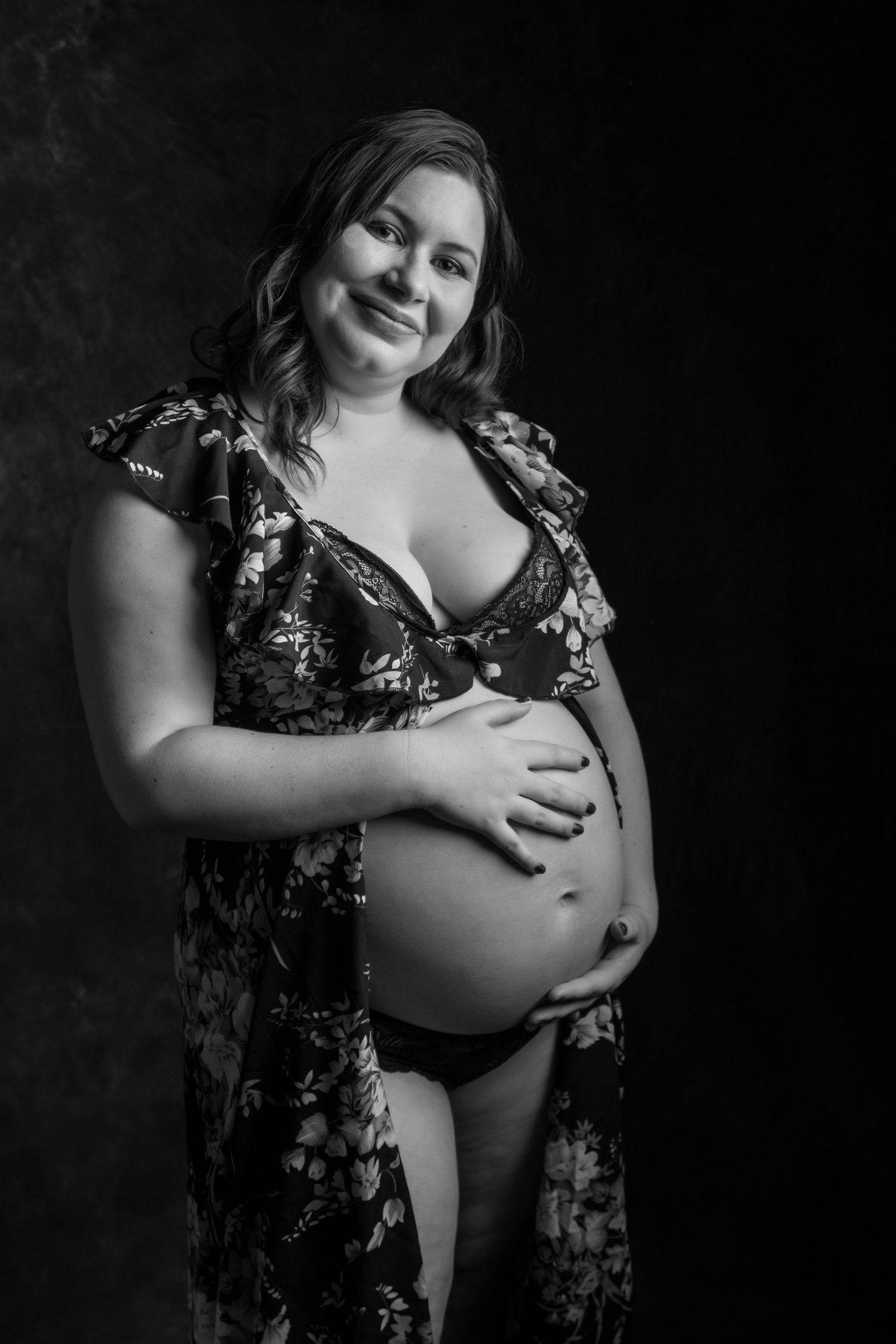 Smiling pregnant woman in floral robe and lingerie cradling her baby bump. Boudoir photography Christchurch maternity