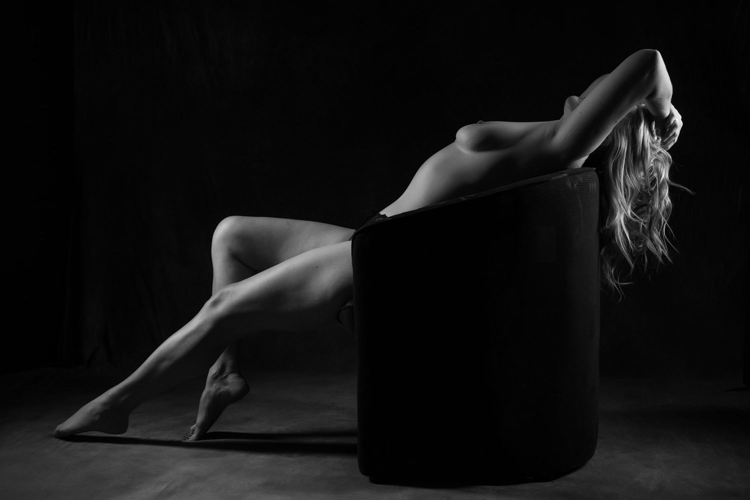 Artistic black and white nude silhouette of a woman reclining gracefully against a dark background. Boudoir photography Christchurch