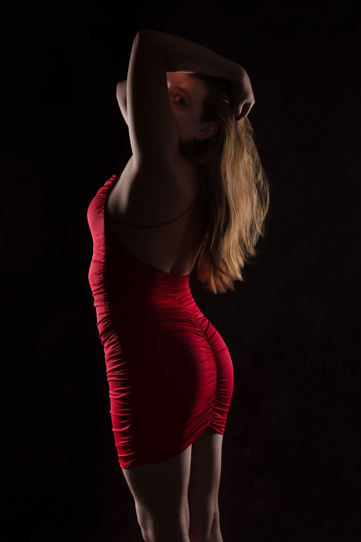 Woman in a tight red backless dress posing against a dark background in low-key lighting. boudoir photography Christchurch
