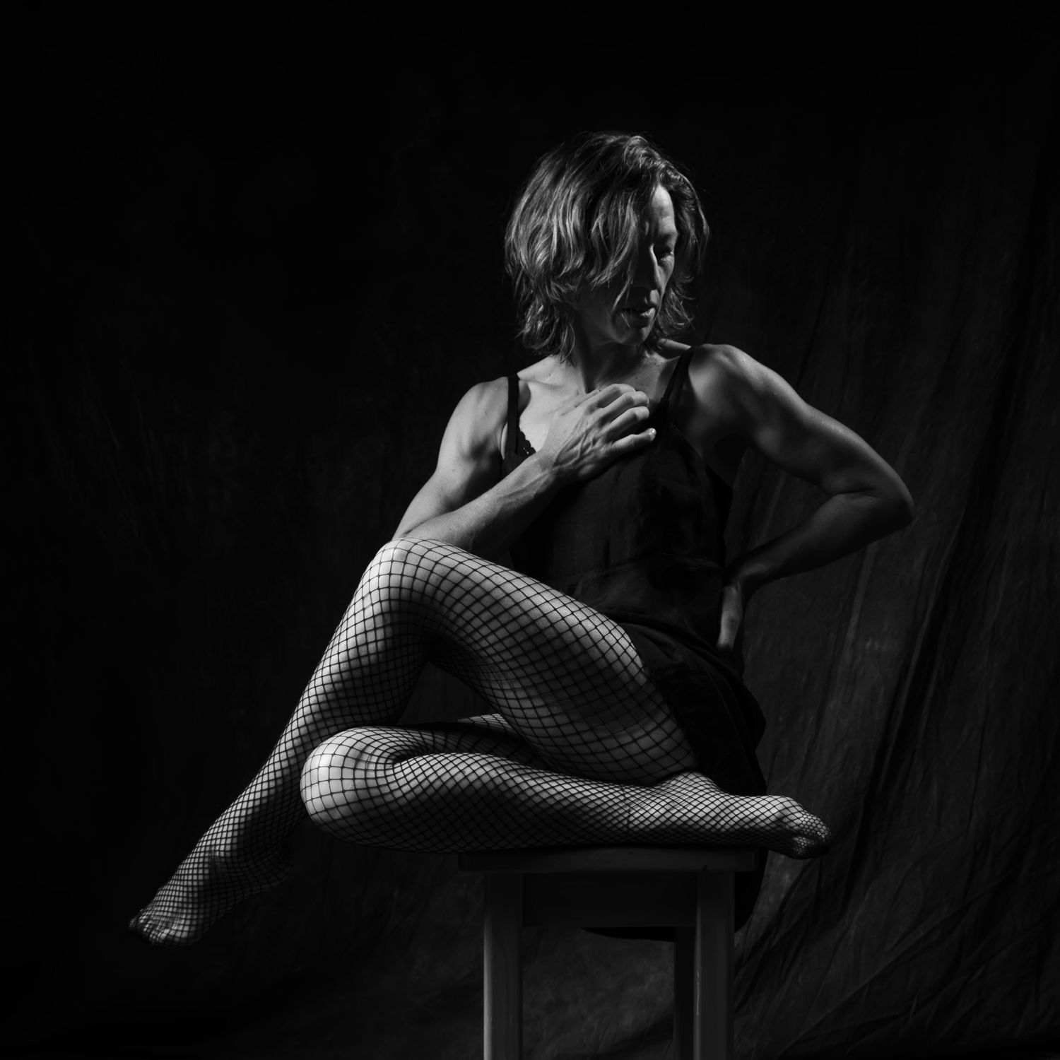 Black and white artistic portrait of a muscular woman in fishnet tights seated on a chair. Boudoir photography Christchurch