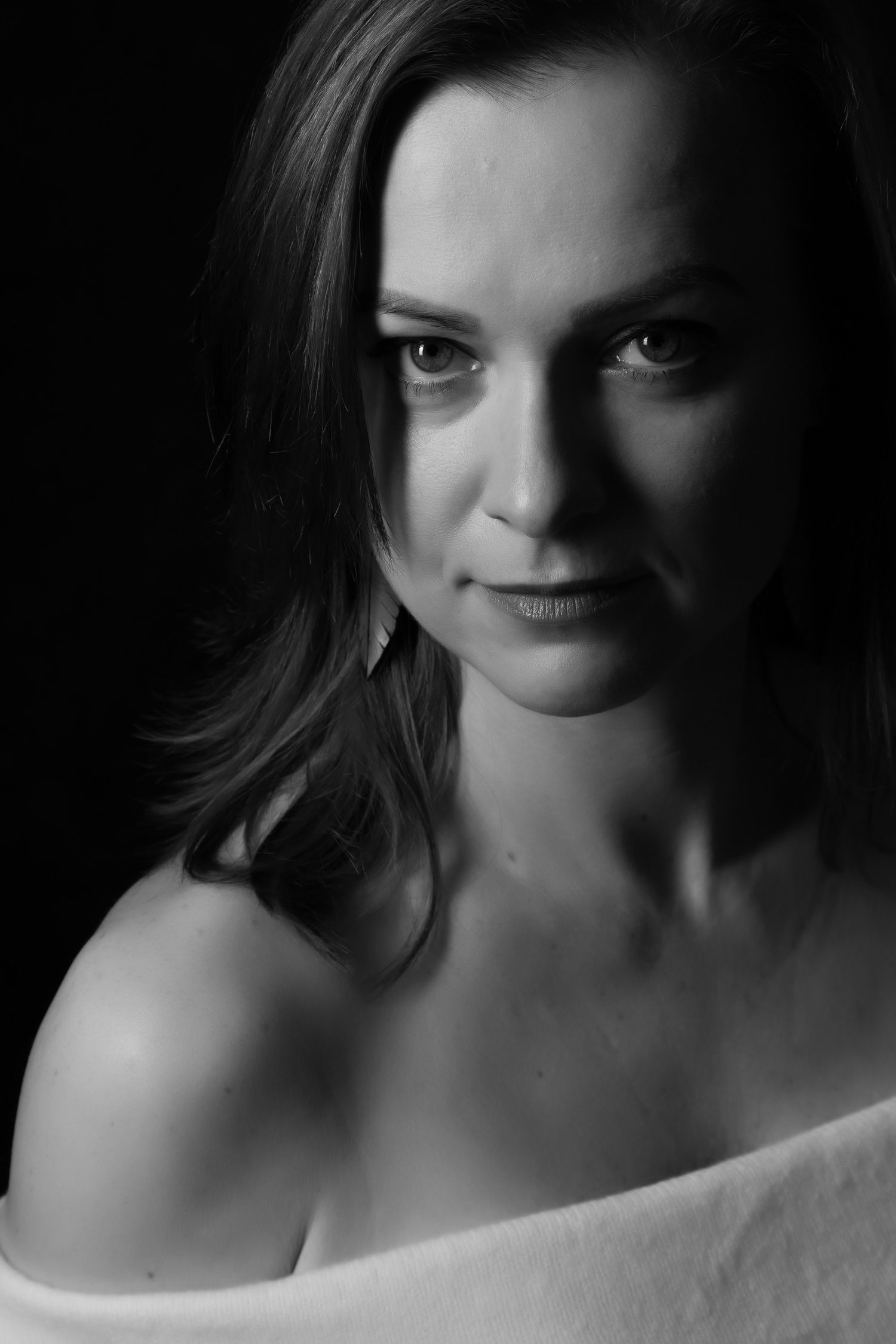 Black and white low-key portrait of a brunette woman with bare shoulders looking directly at camera. boudoir photography Christchurch