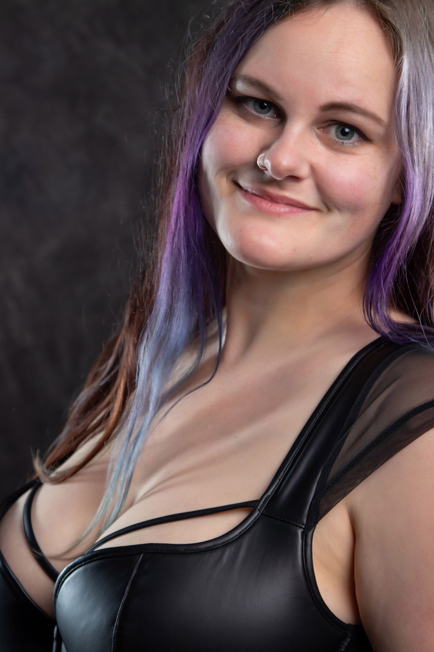 Smiling woman with purple hair wearing a black leather corset in a studio portrait. Boudoir photography Christchurch