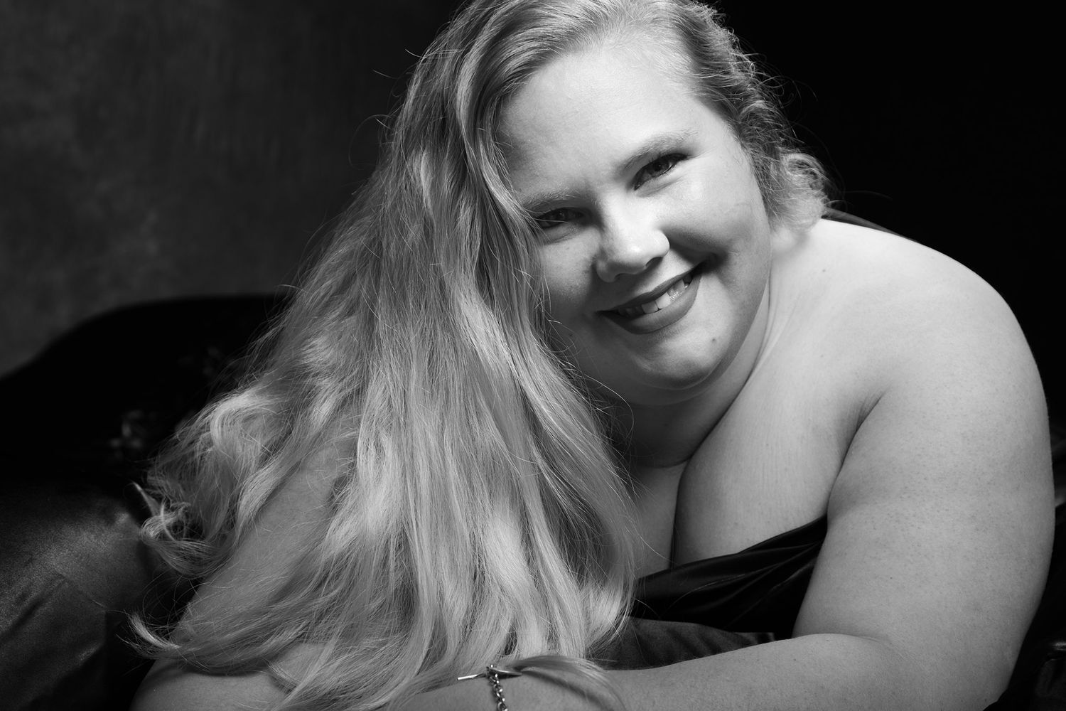Black and white portrait of a smiling plus-size blonde woman posing elegantly in a boudoir photography session. Boudoir photography Christch
