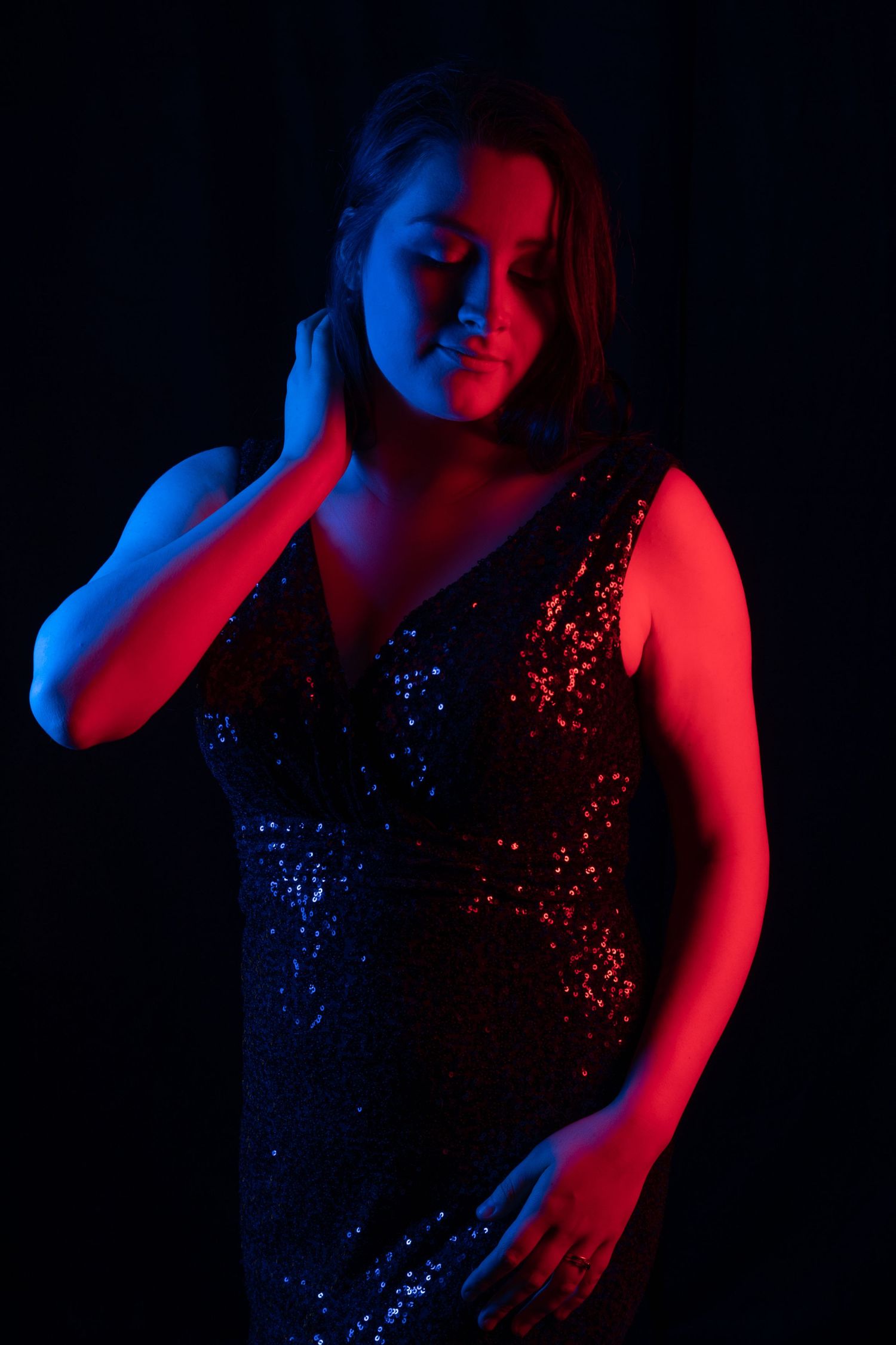 Woman in a sequined dress posed dramatically under blue and red neon studio lighting.