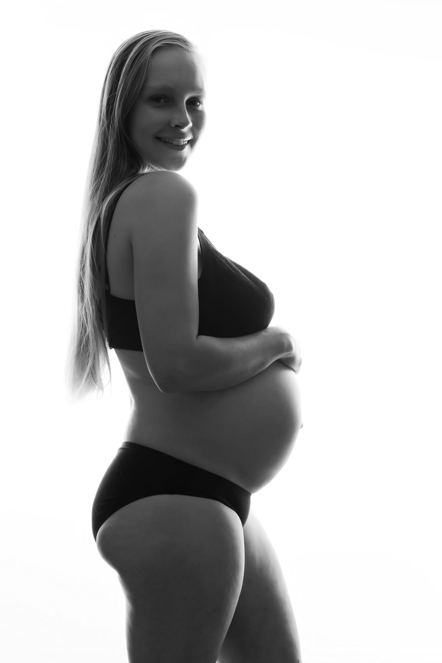 Black and white maternity photo of smiling pregnant blonde woman in lingerie holding baby bump. Boudoir photography Christchurch maternity