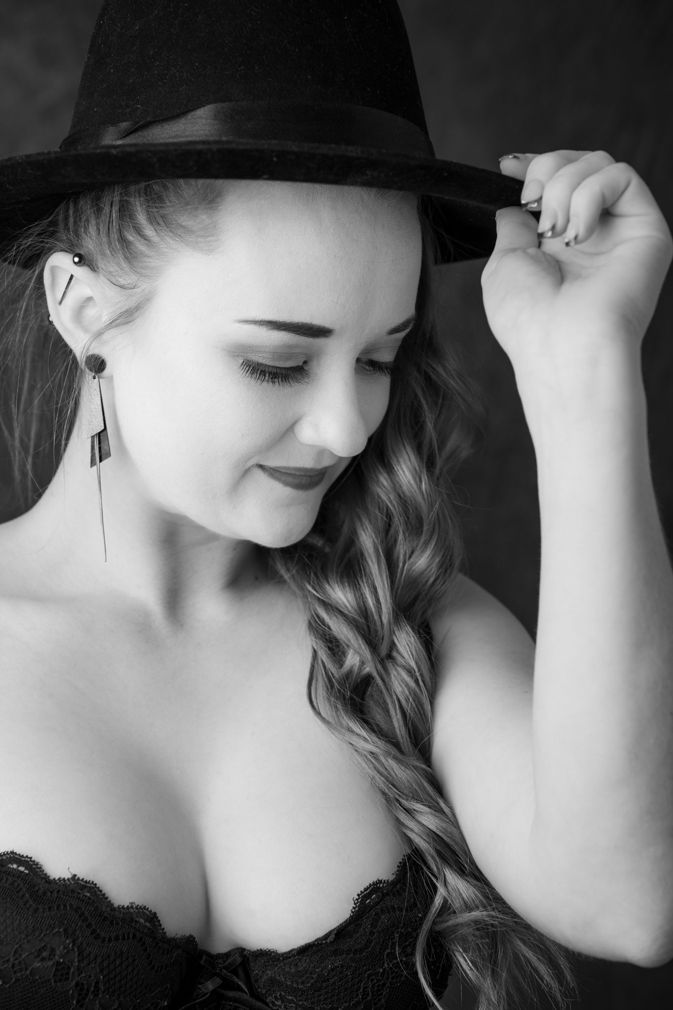 Black and white portrait of a young woman in lace top corset holding a black fedora hat with braided hair. Boudoir photography Christchurch