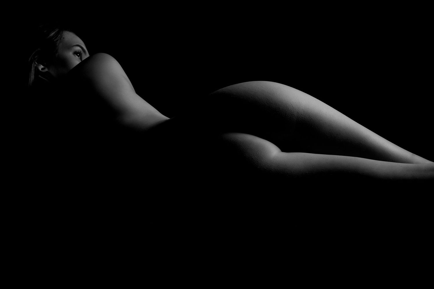 Artistic black and white silhouette of a reclining nude woman against a dark background. Boudoir photography Christchurch bodyscape