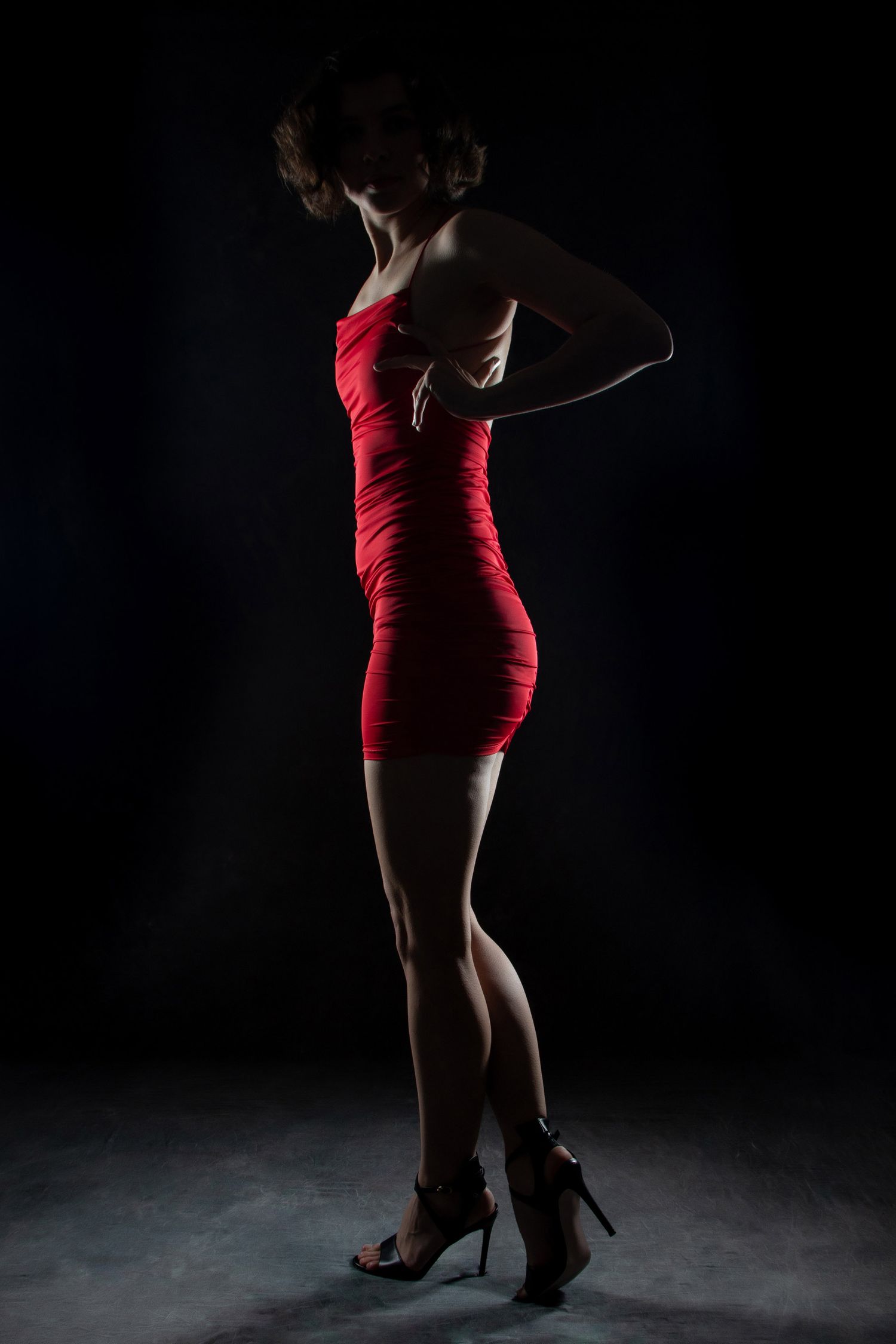 Woman in a tight red mini dress and heels posing in dramatic low-key studio lighting. Boudoir photography Christchurch portrait