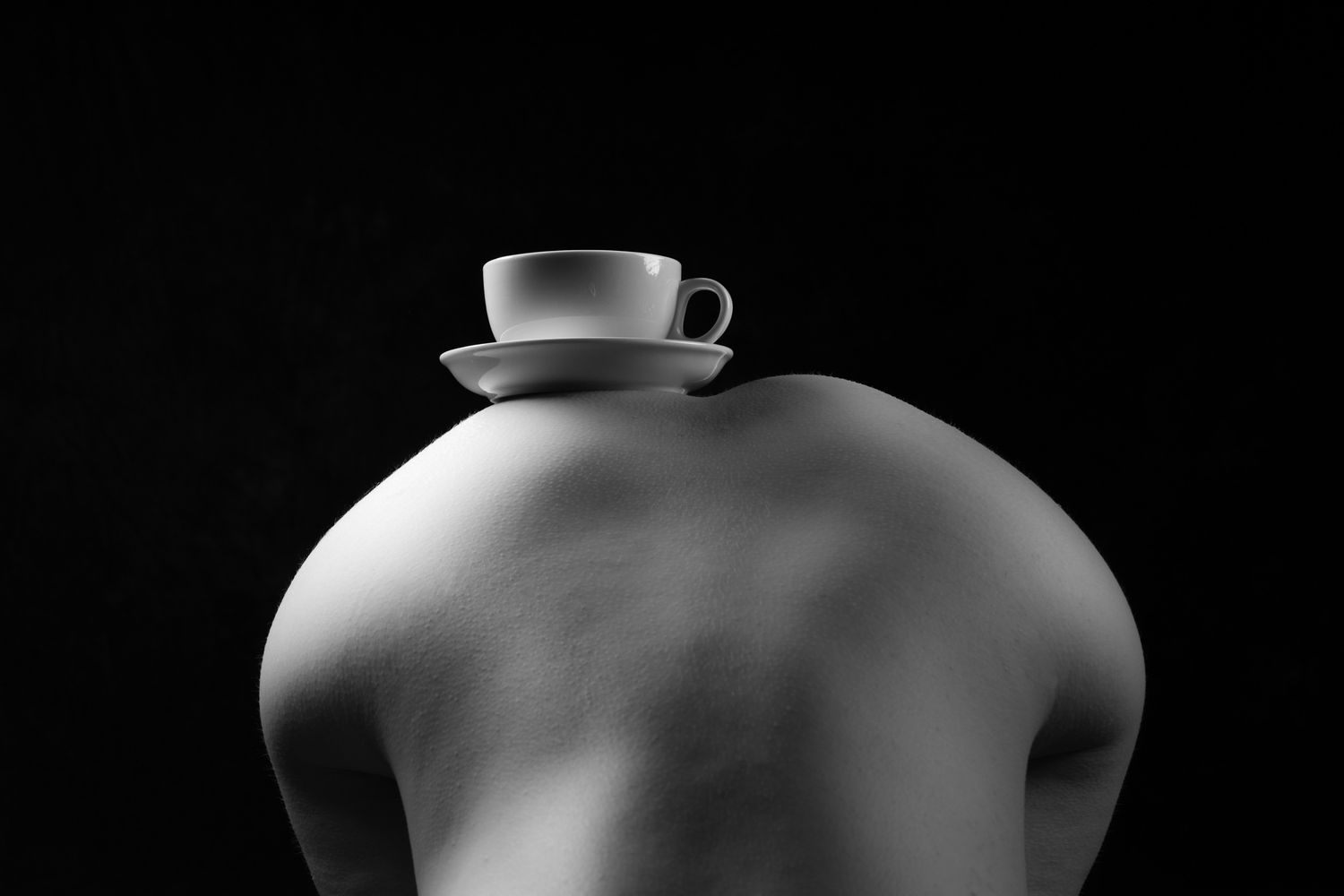 Black and white artistic photo of a persons bare behind with a white teacup and saucer balanced on top. Boudoir photography Christchurch
