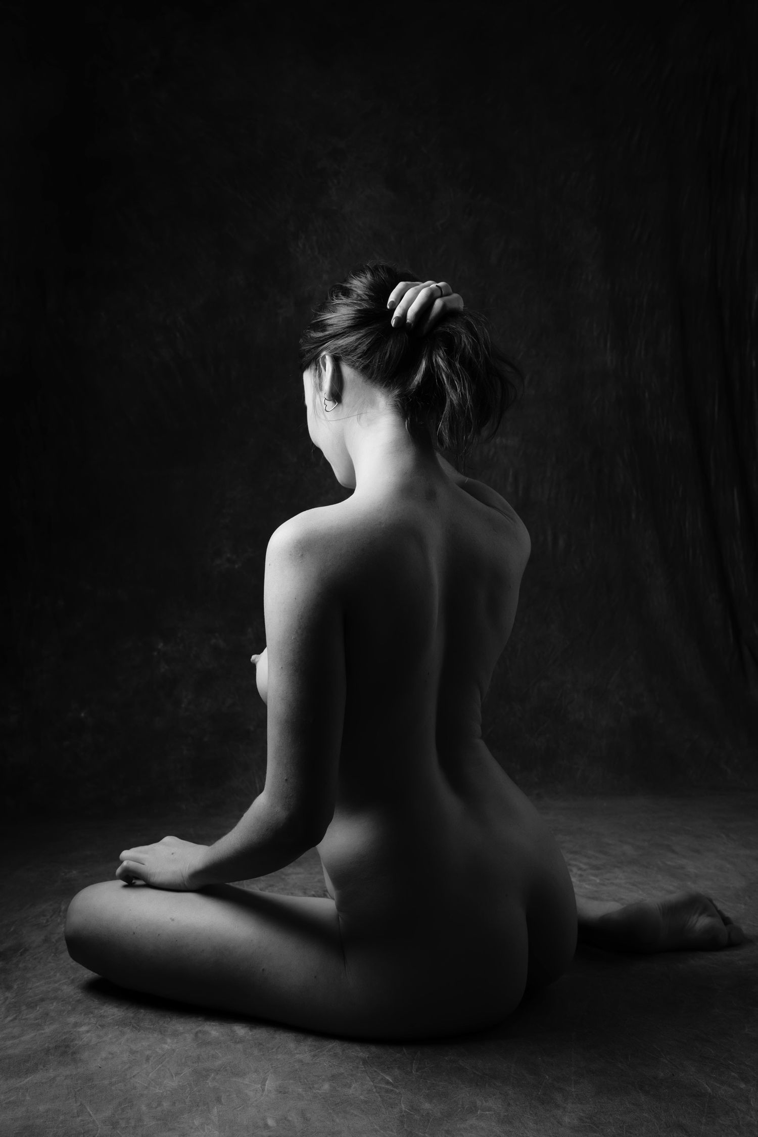 Artistic black and white nude fine art photograph of a woman seated cross-legged, shot from behind in studio. Boudoir photography Christchur