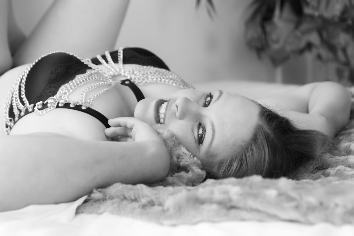Black and white boudoir portrait of a smiling woman in decorative lingerie lying on a soft surface. Boudoir photography Christchurch