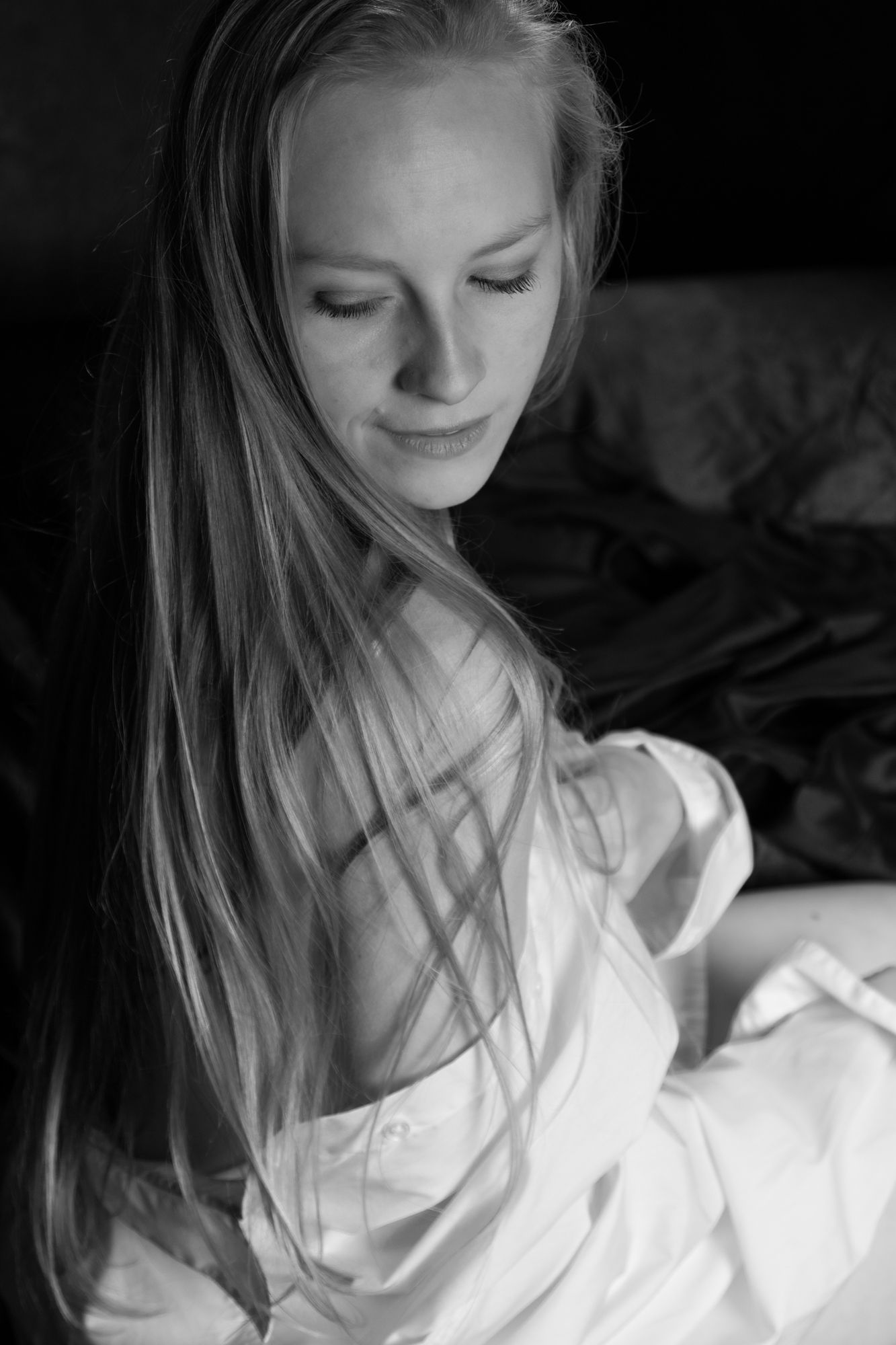 Blonde woman with long hair in a white shirt looking down in a soft black and white portrait. Boudoir photography Christchurch