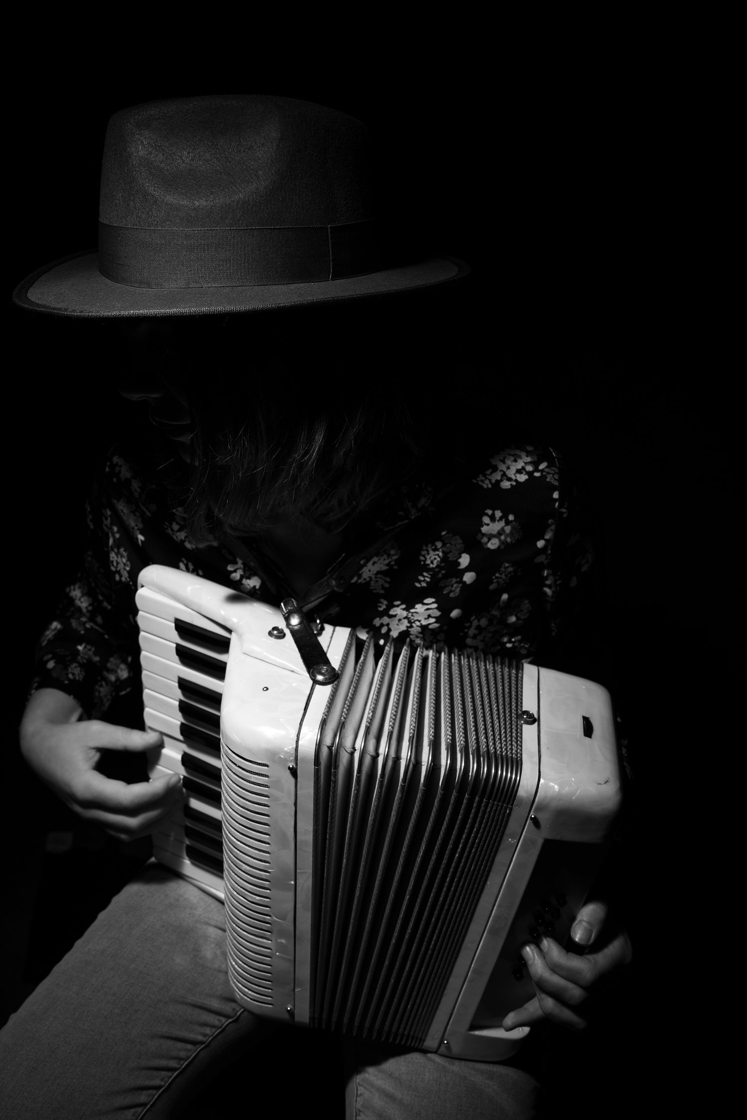 Black and white photo of a person in a hat playing accordion against a dark background. portrait photography Christchurch