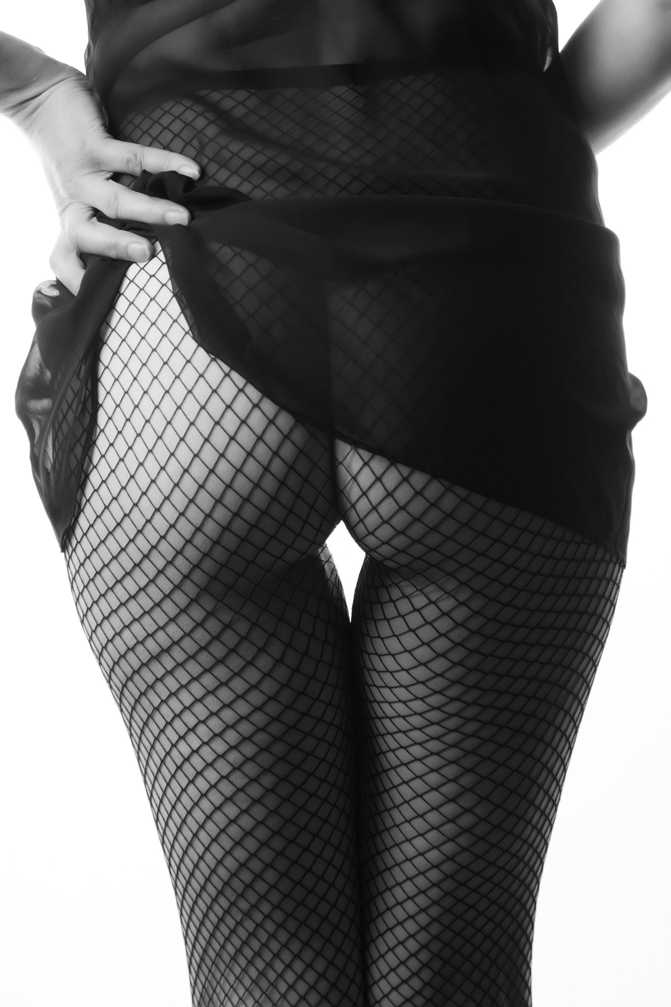 Black and white close-up of a woman wearing fishnet stockings and a black wrap skirt with hand on hip. Boudoir photography Christchurch