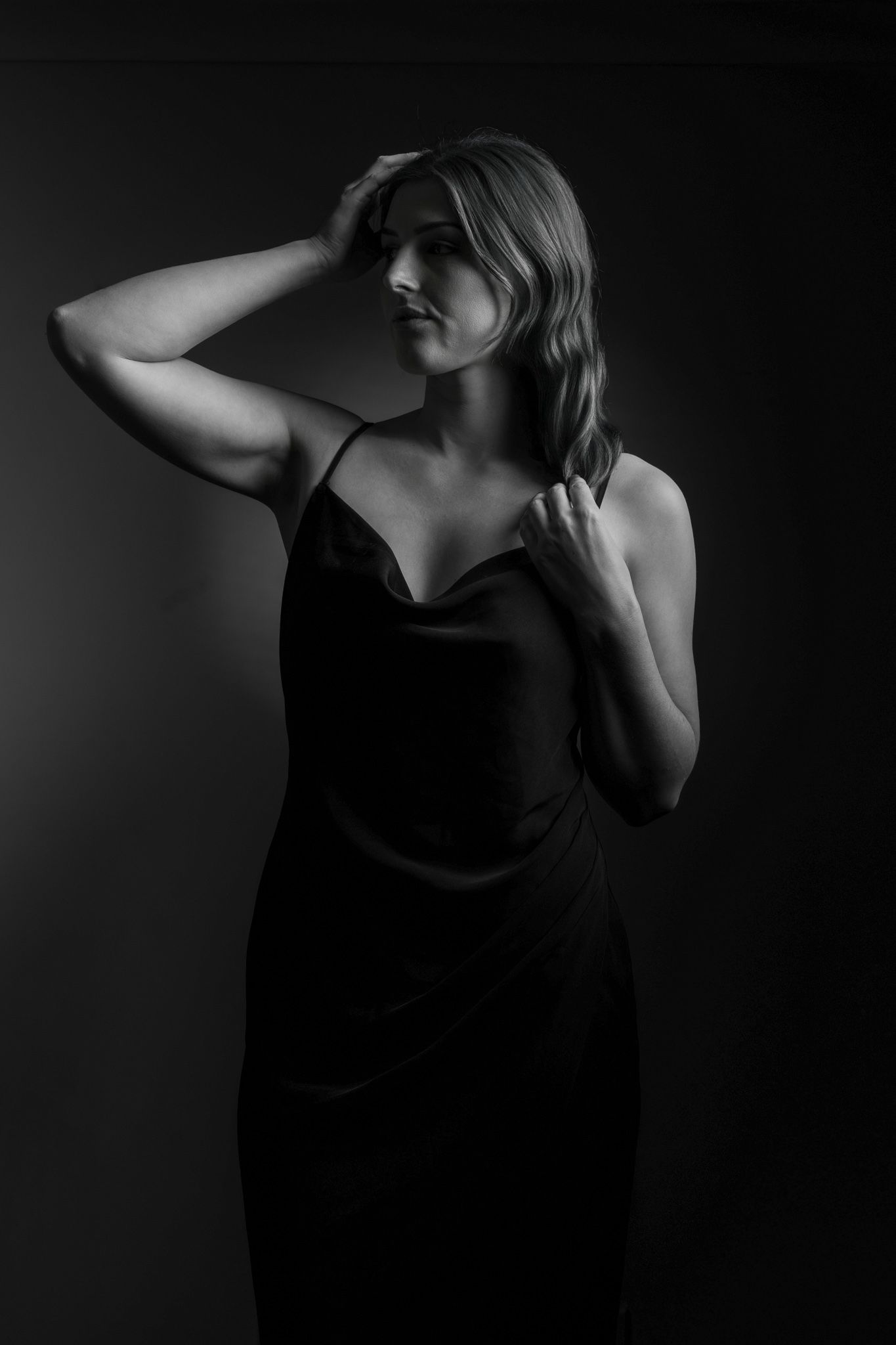 Black and white studio portrait of a woman in a black slip dress with hands in hair. portrait photography Christchurch