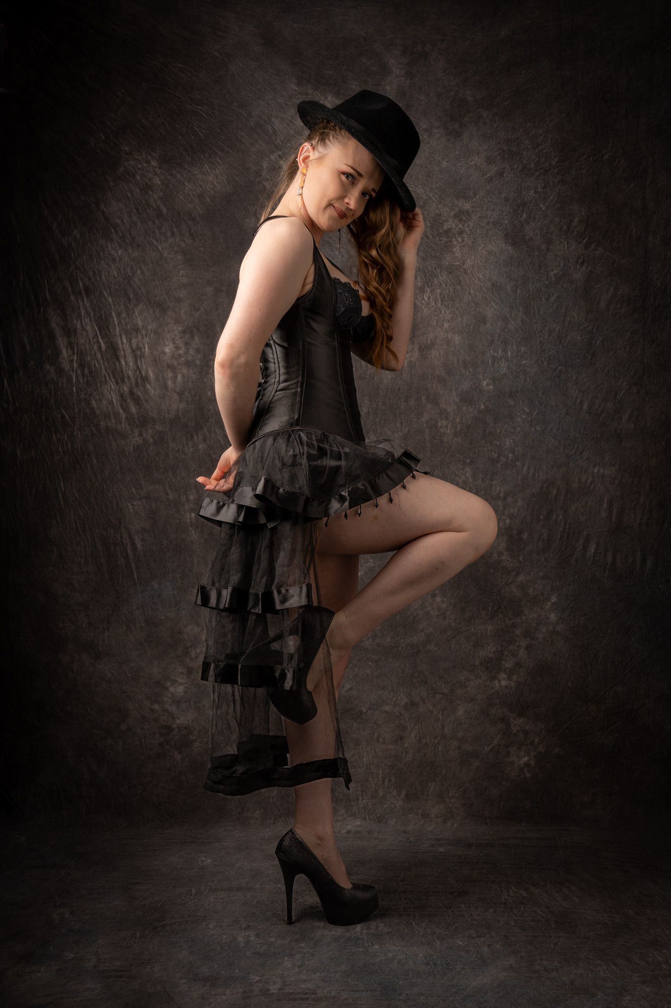 Woman in black corset dress and fedora hat posing in dramatic studio portrait. Boudoir photography Christchurch