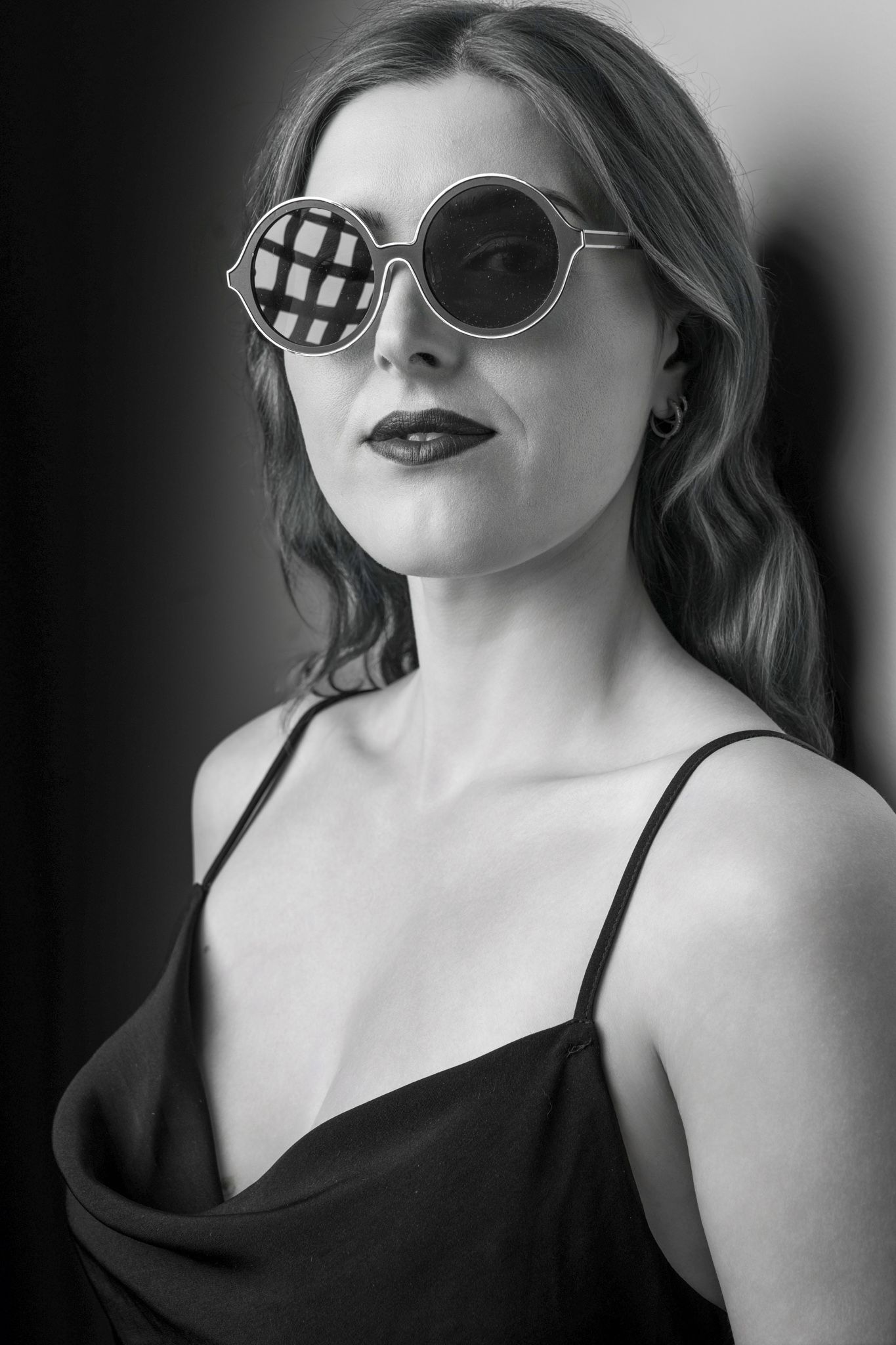 Black and white portrait of a woman wearing unique round grid-patterned sunglasses and black slip dress. portrait photography Christchurch