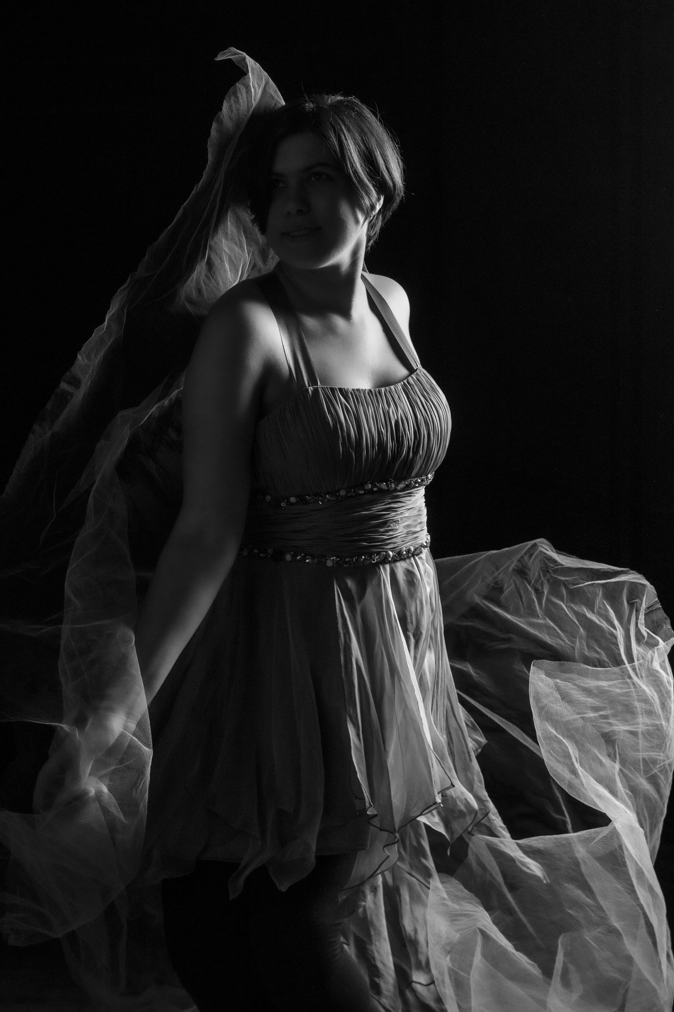 Black and white portrait of a woman in a flowing dress with billowing fabric against a dark background. portrait photography Christchurch