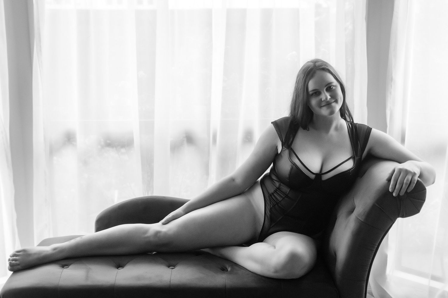Plus-size woman in black lingerie reclining on a chaise lounge in a boudoir photo session. Boudoir photography Christchurch