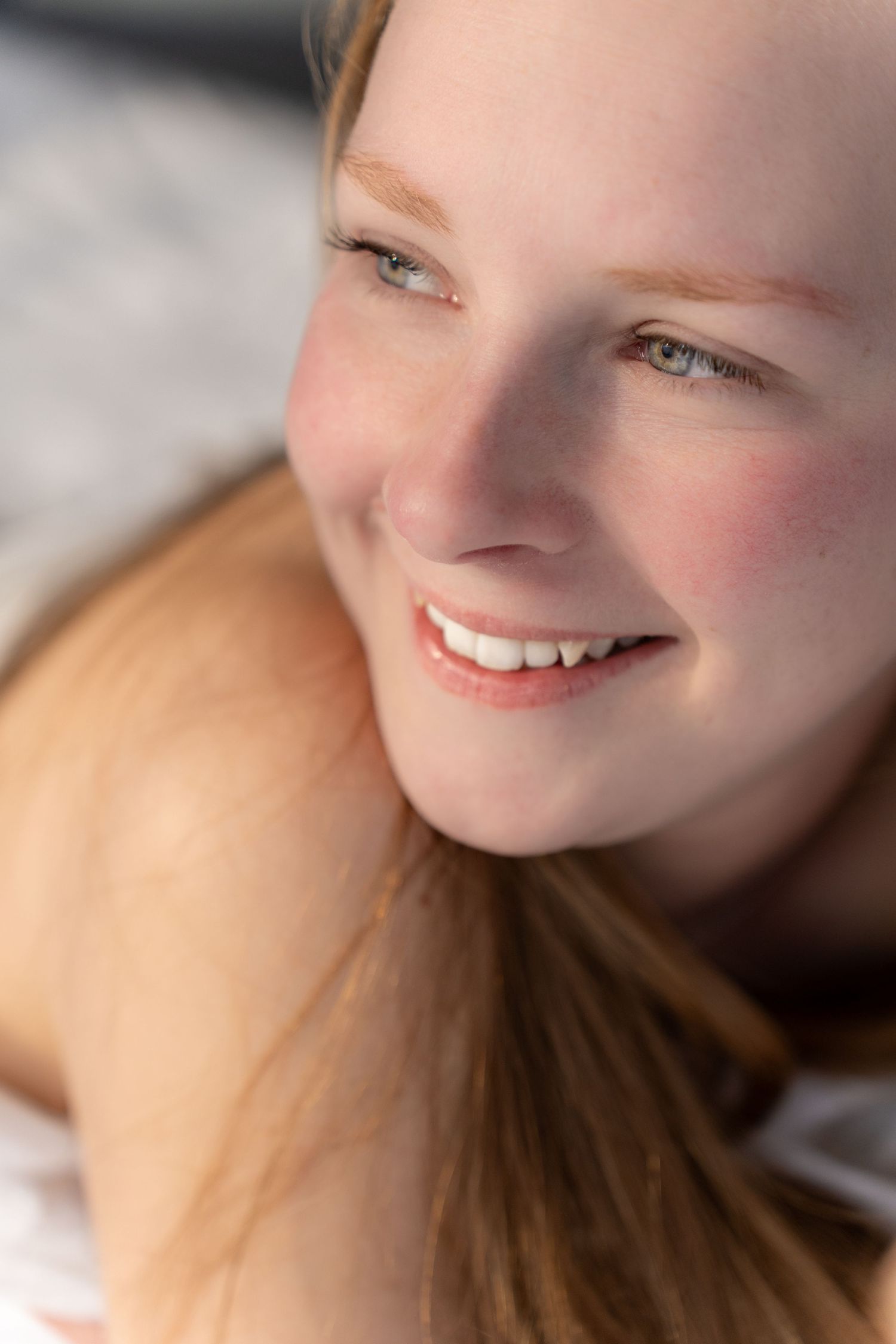 Smiling young woman with red hair and blue eyes looking up, bathed in natural sunlight.