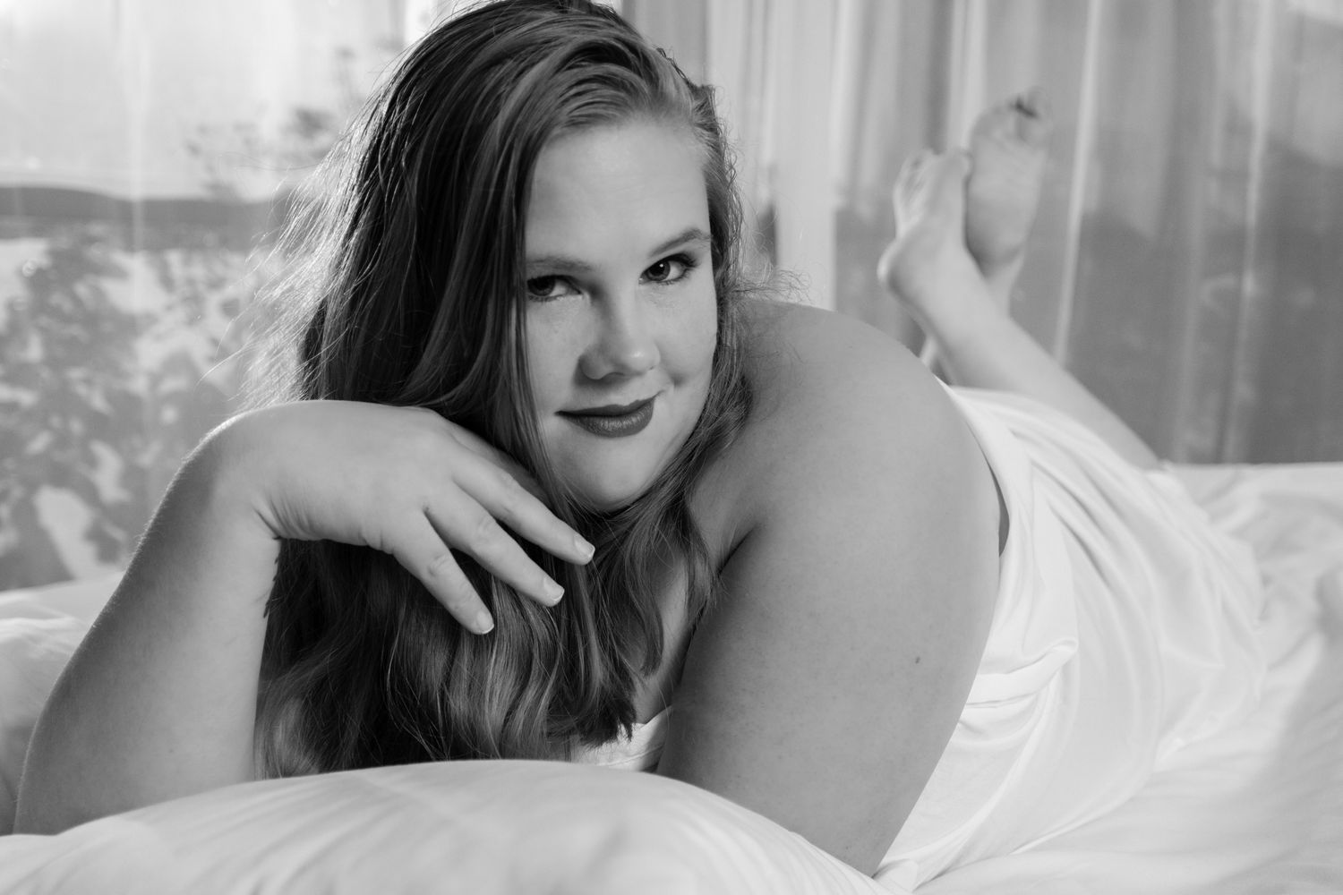 Smiling woman lying on white bed posing, elegant black and white boudoir photography. Boudoir photography Christchurch