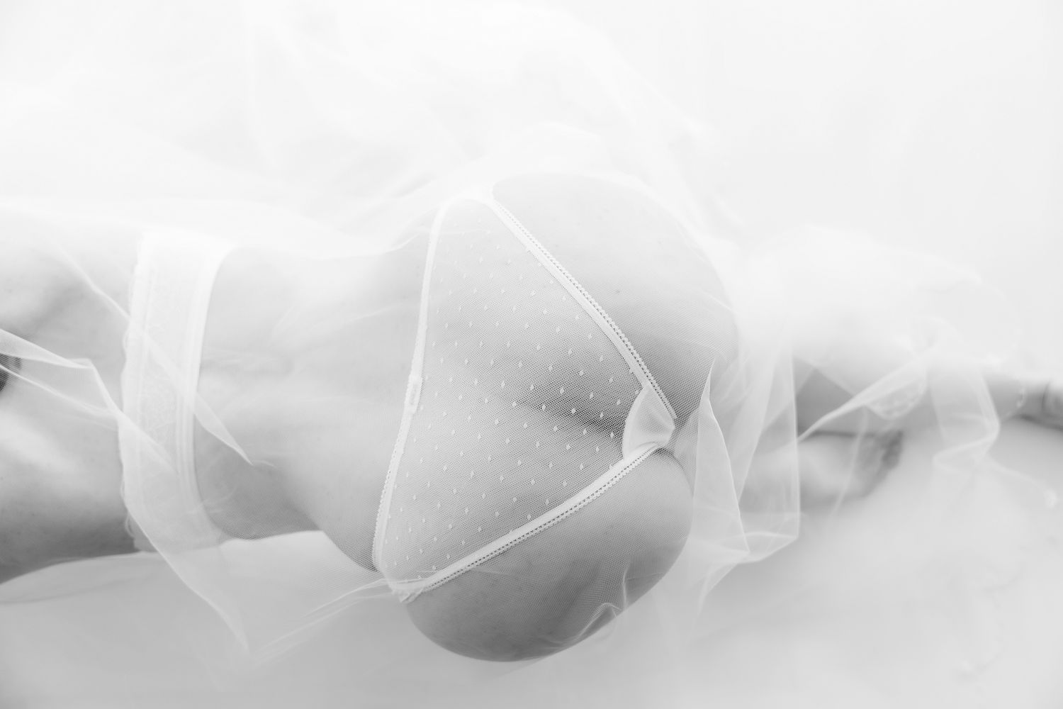 Black and white artistic photo of a woman's body draped in flowing sheer white fabric. Boudoir photography Christchurch
