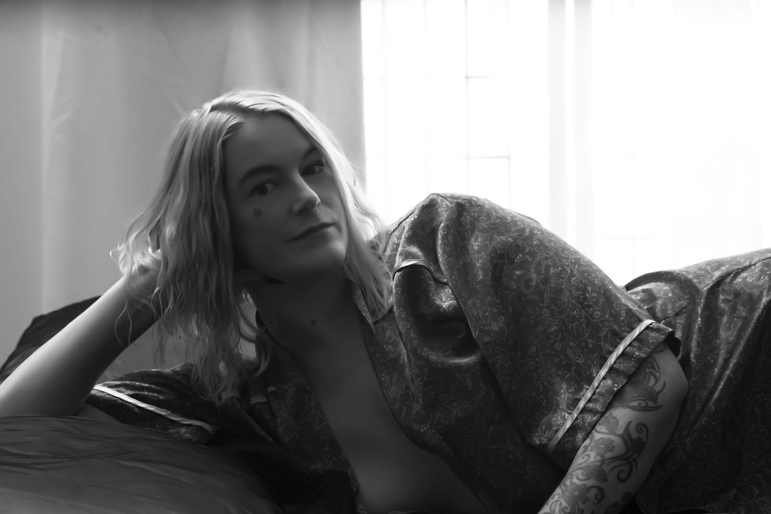 Black and white boudoir portrait of a blonde woman reclining on a sofa by a window. boudoir photography Christchurch