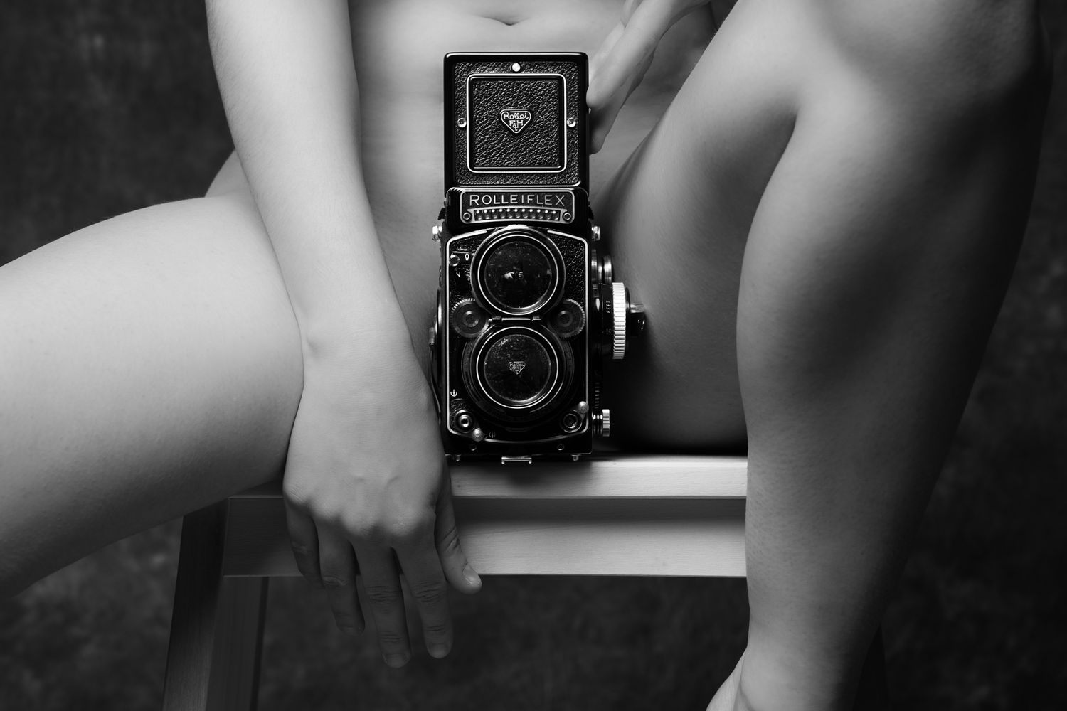 Black and white photo of nude woman with hands holding a vintage Rolleiflex twin-lens reflex camera. Boudoir photography Christchurch